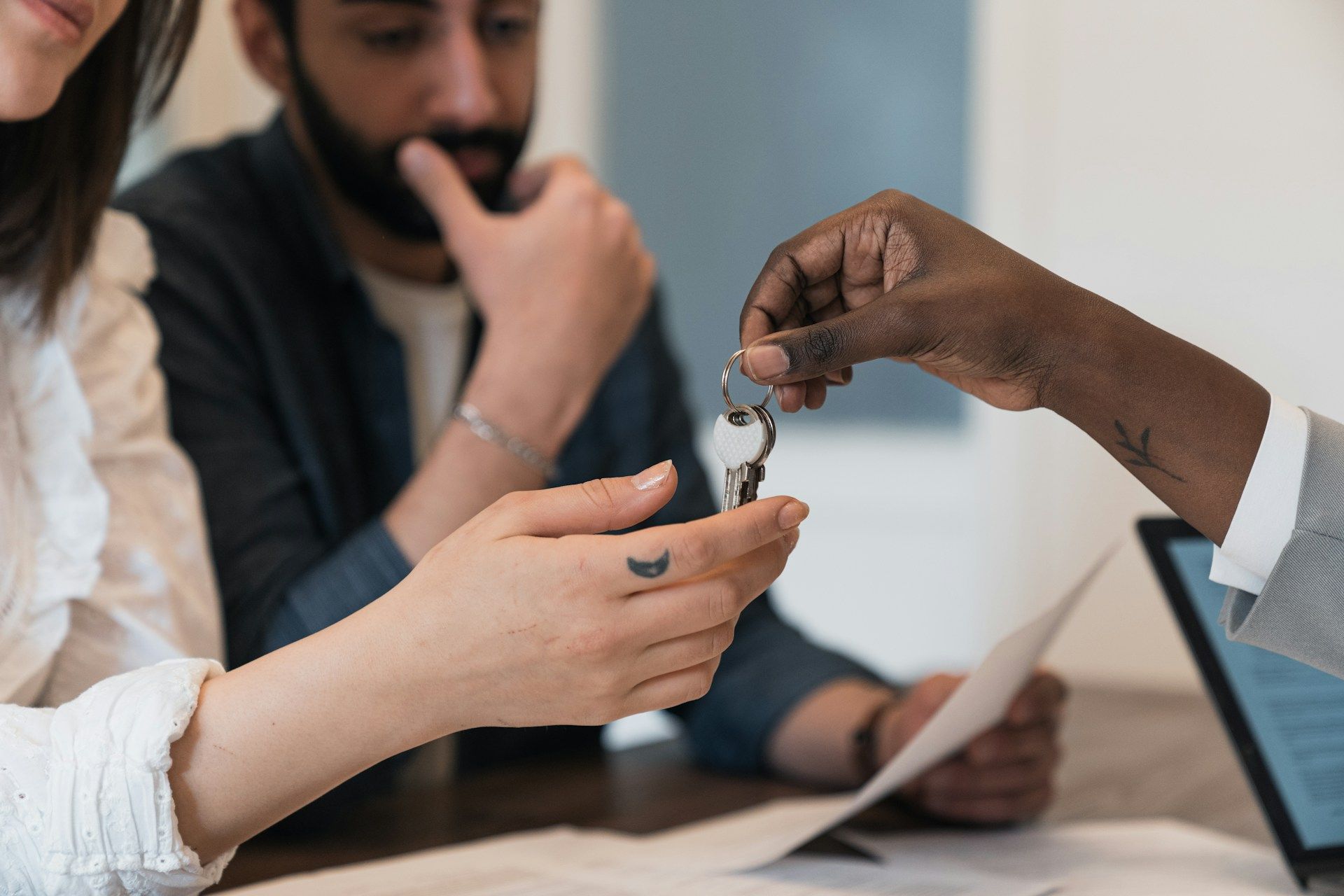 Person handing keys to another person, couple in background, sitting at a table.