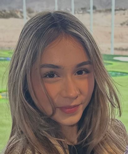 Woman with light brown hair, smiling, in front of a golf course, wearing a black shirt.