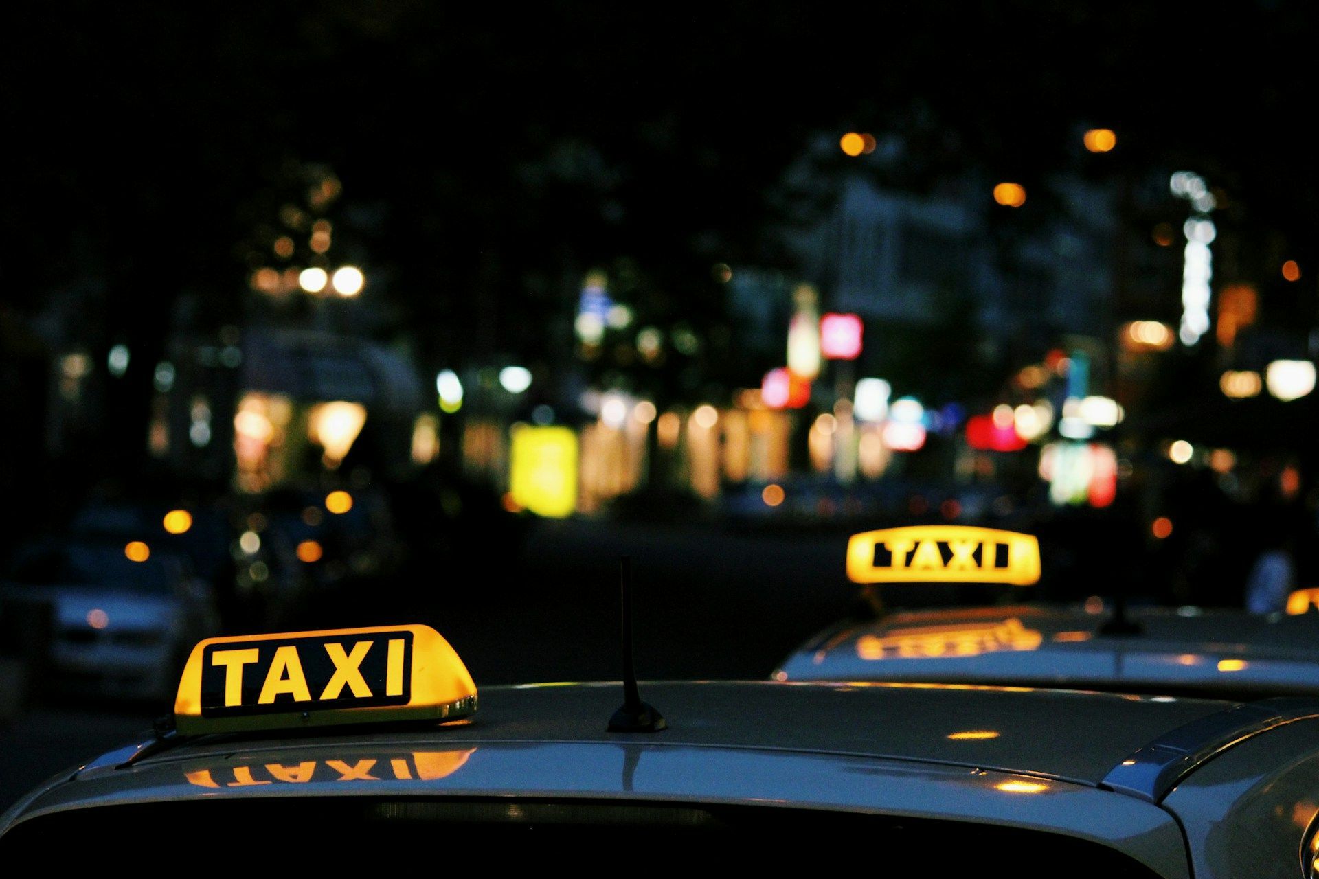 Taxi cabs with lit rooftop signs against a blurry, night city background.