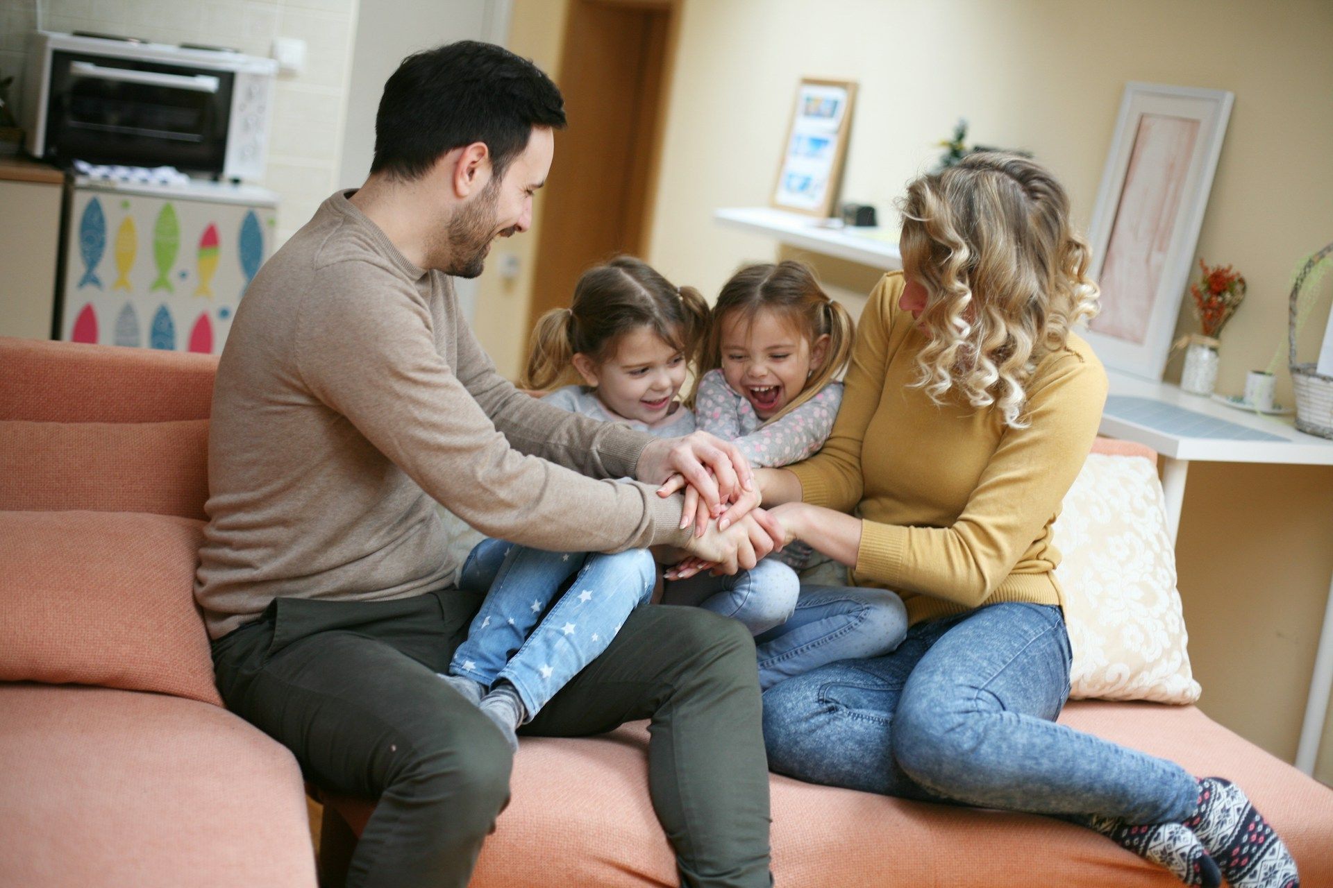 Family of four huddled together on a couch, hands in a pile, smiling.