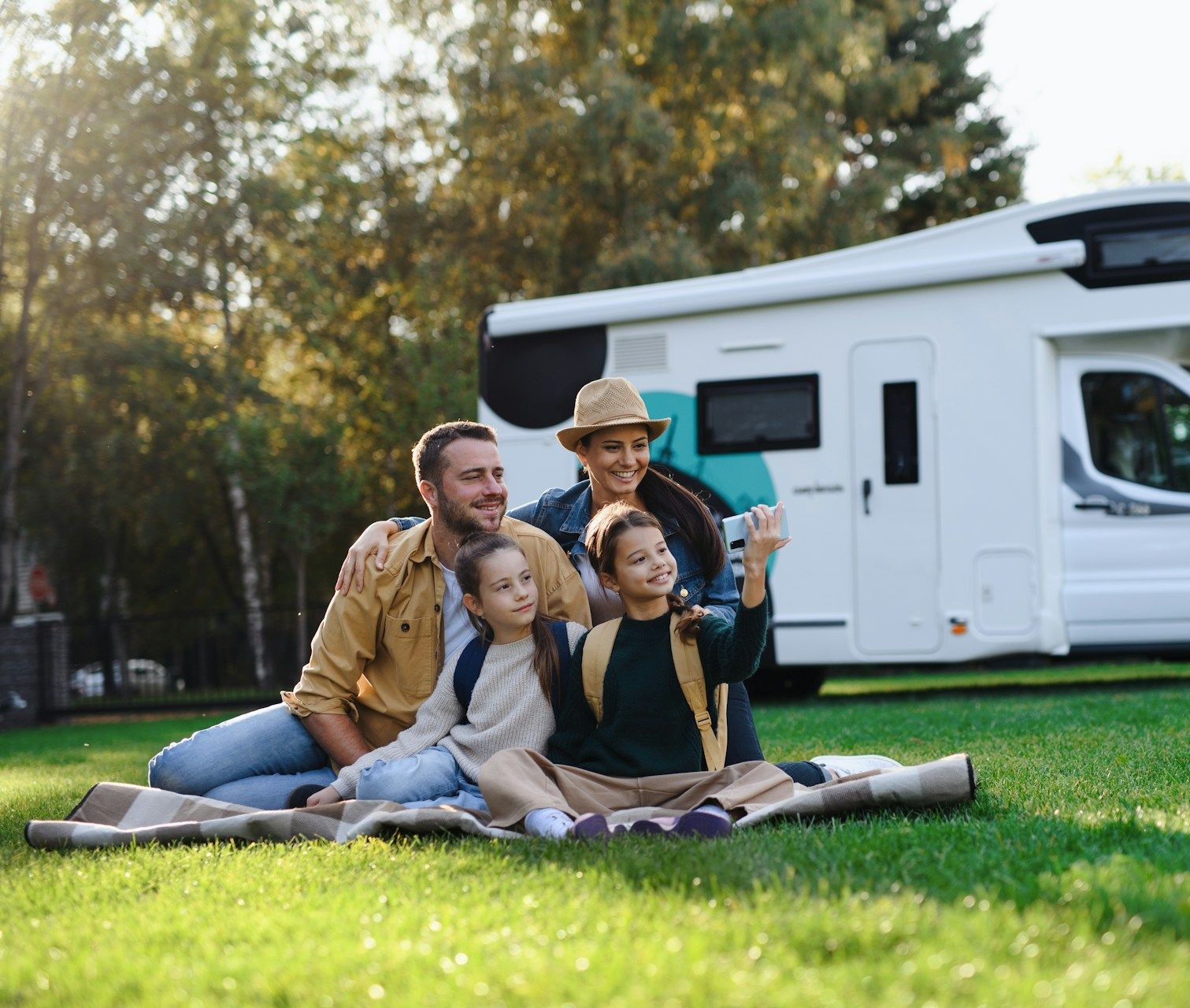 Family seated on a blanket in front of an RV, smiling.