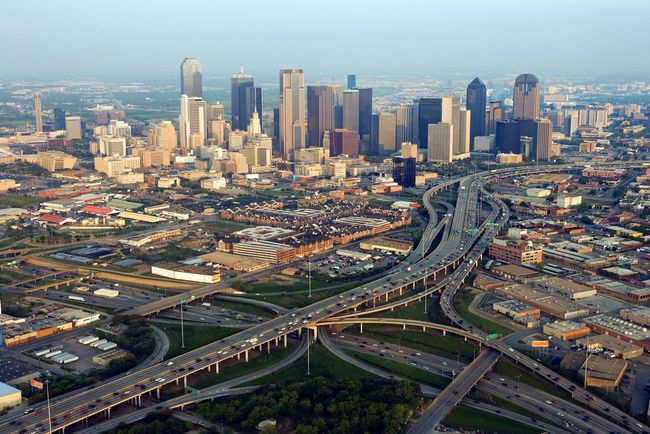 Aerial view of Dallas, Texas, with numerous skyscrapers and a complex network of highways.
