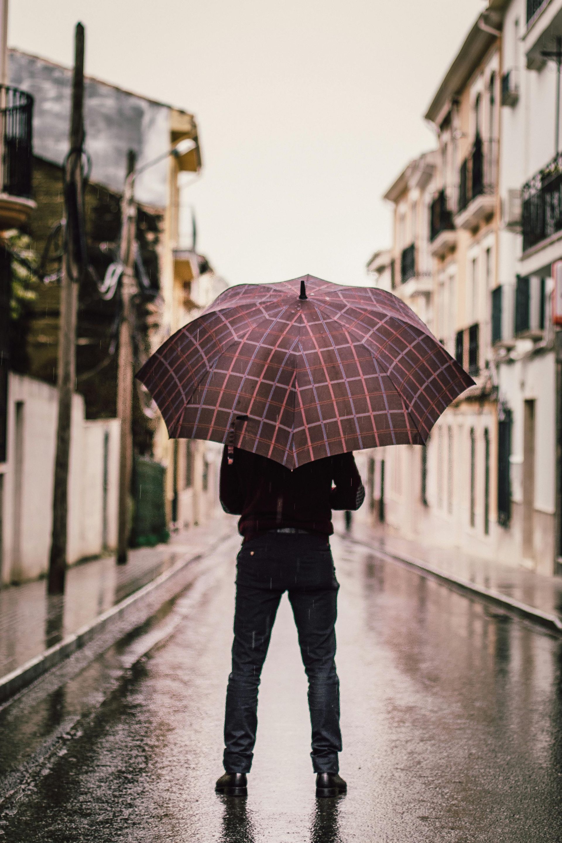 Person standing in a wet street, holding a patterned umbrella, buildings in background.