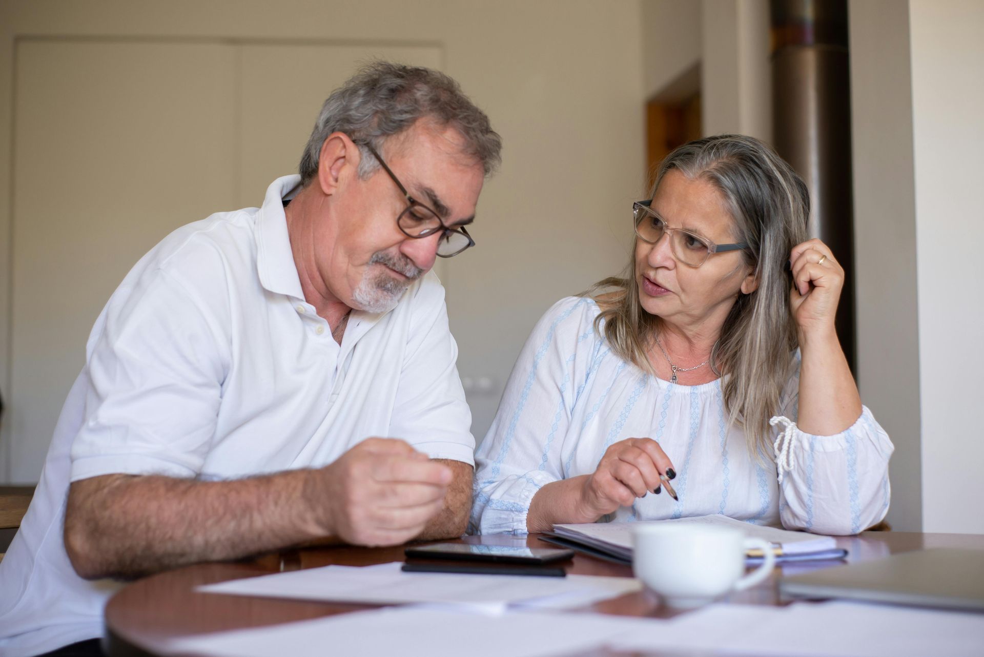 Couple reviews documents and calculator at a table. Woman gestures, man looks at papers.