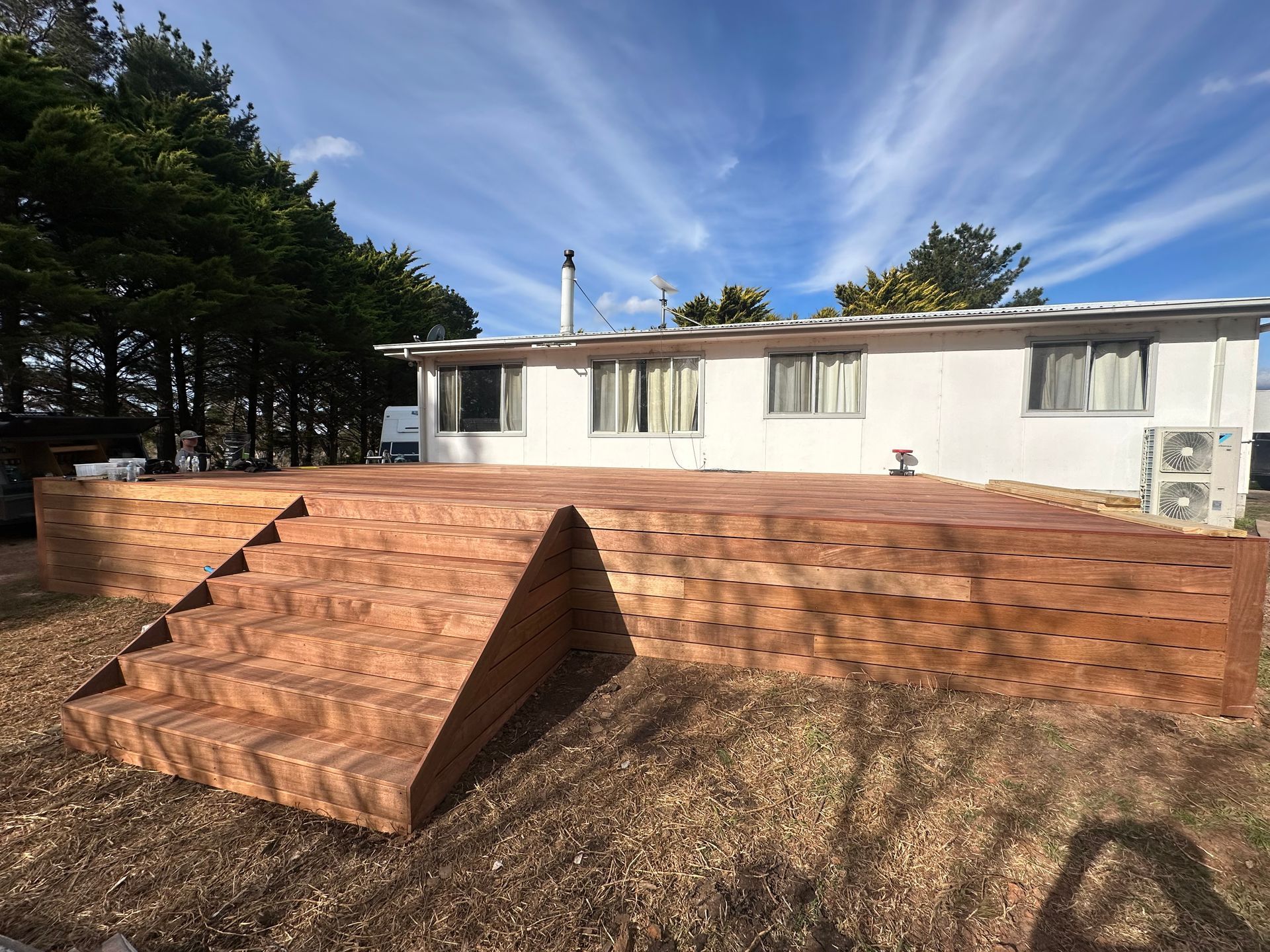 A wooden deck with steps in front of a white house, under a blue sky with clouds — LD Carpentry in Goulburn, NSW