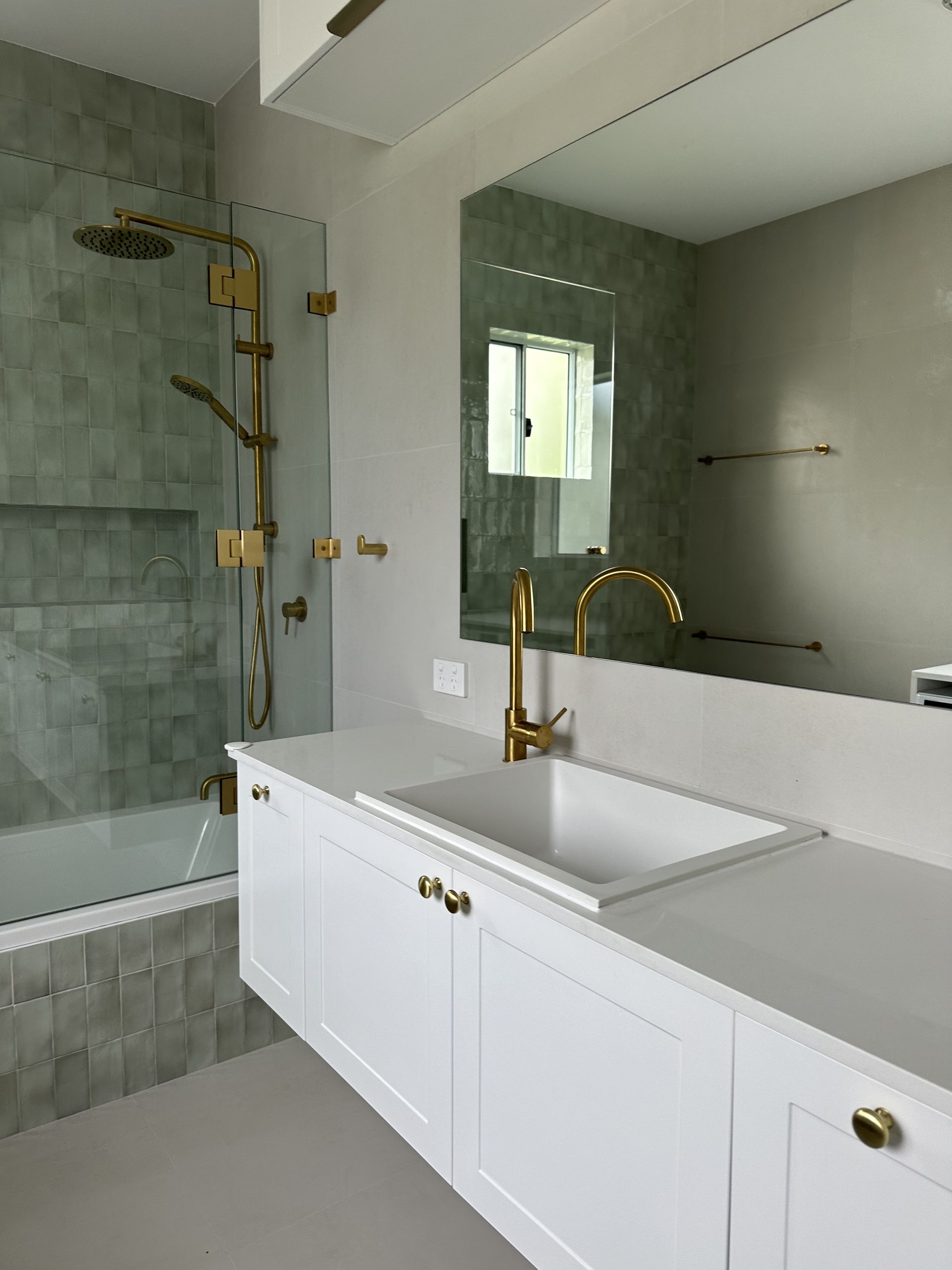 A modern bathroom with gold fixtures, white vanity, and a large mirror — LD Carpentry in Goulburn, NSW