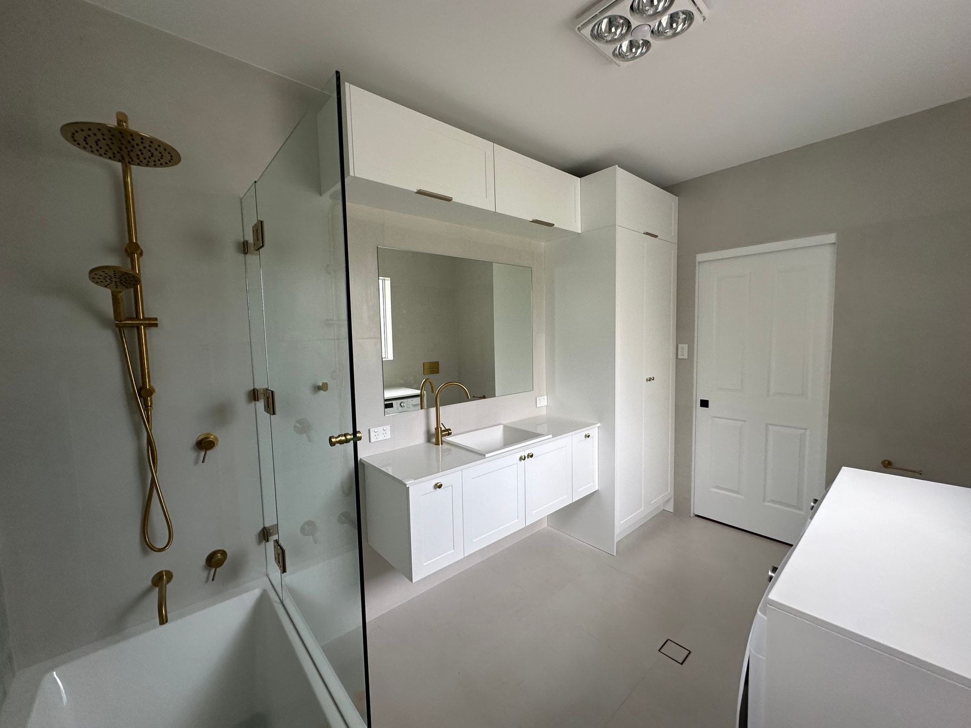 Modern white bathroom with gold fixtures. Features a shower, vanity, and storage — LD Carpentry in Goulburn, NSW