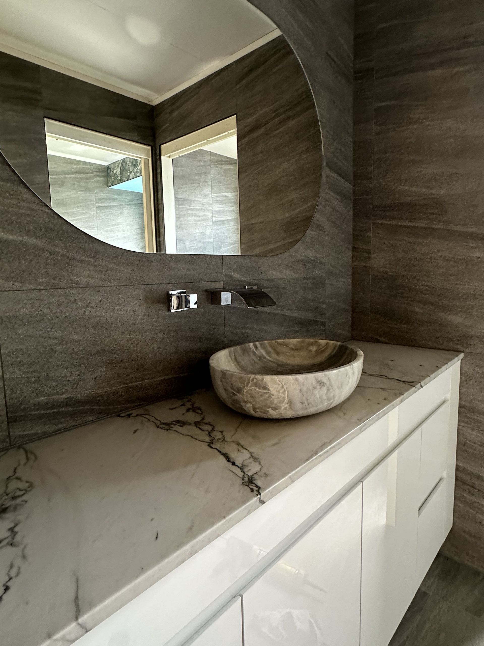 Bathroom with a marble countertop, stone sink, and round mirror — LD Carpentry in Goulburn, NSW