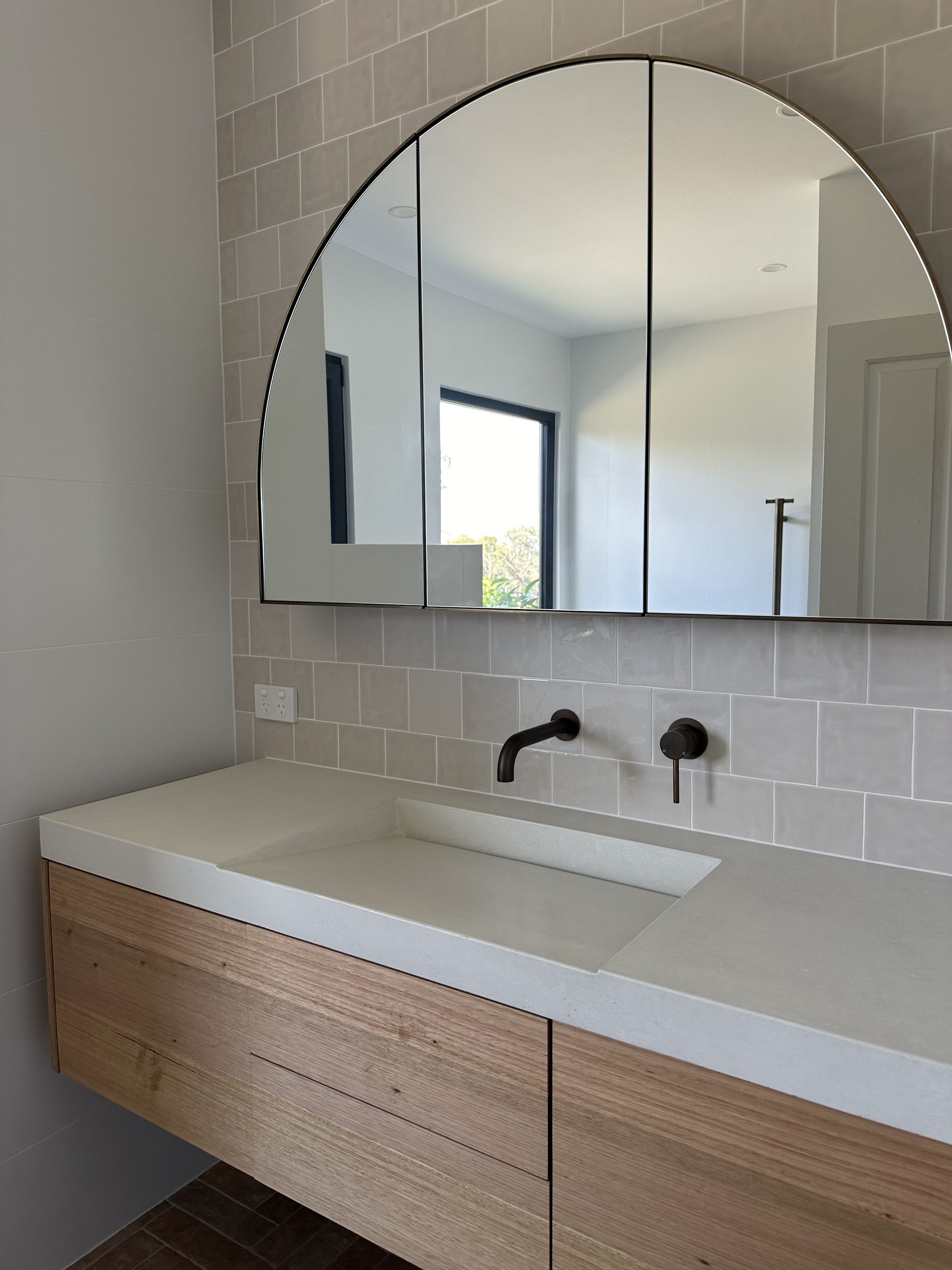 Modern bathroom with an arched mirror, floating wooden vanity, and black fixtures — LD Carpentry in Goulburn, NSW
