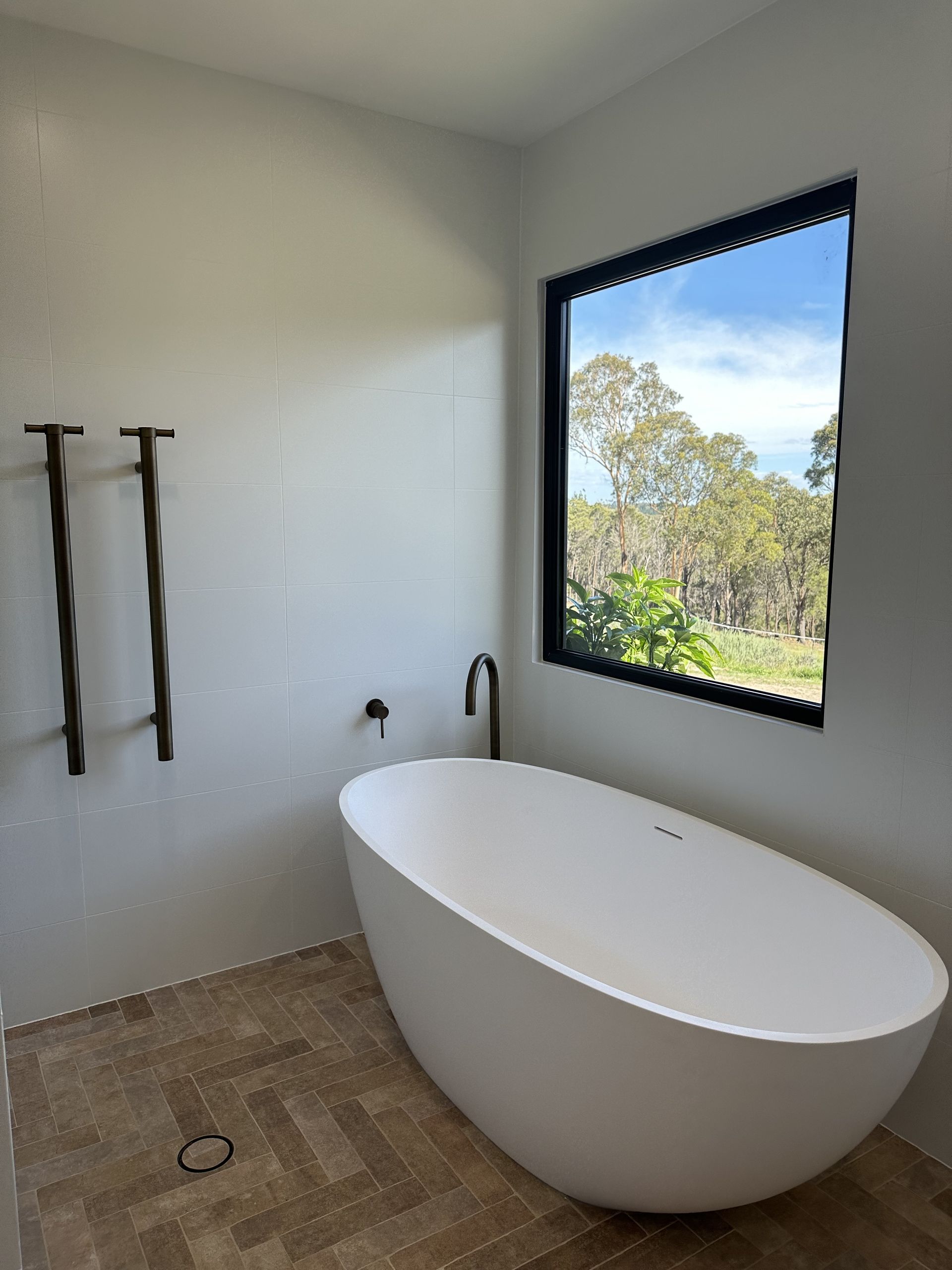 Modern bathroom with a white freestanding tub and black-framed window — LD Carpentry in Goulburn, NSW