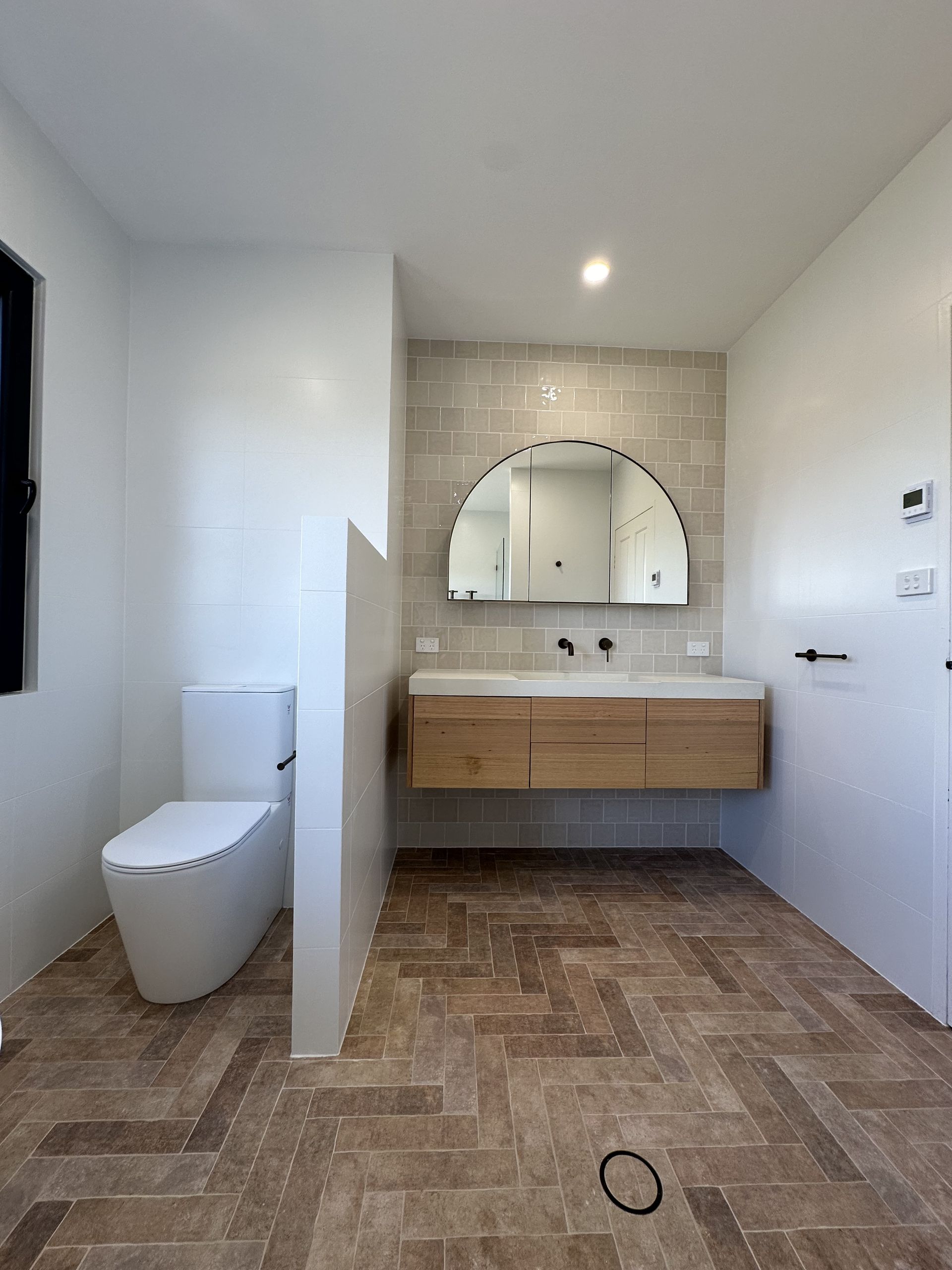 Modern bathroom with a wooden vanity, arched mirror and a white toilet — LD Carpentry in Goulburn, NSW