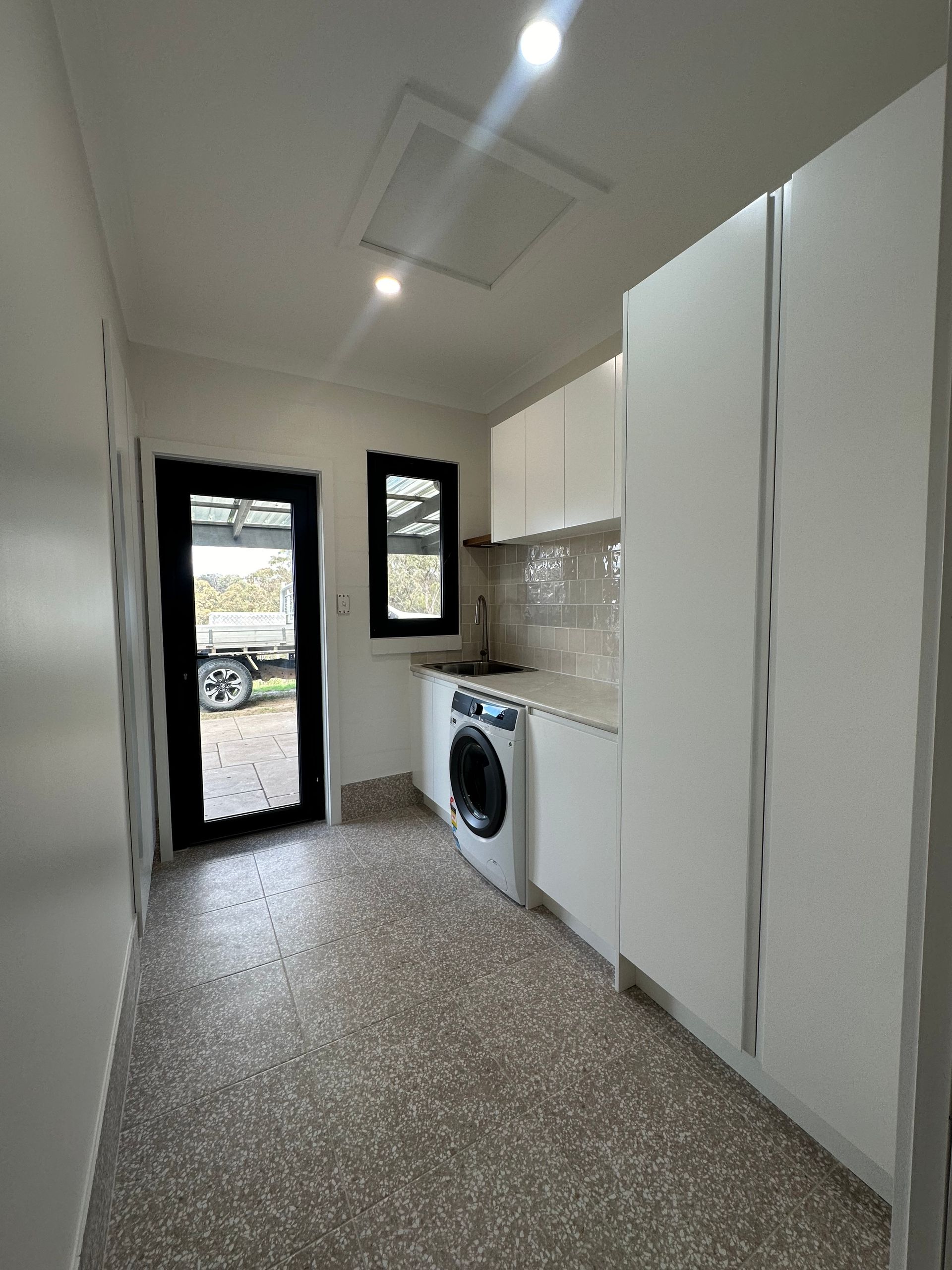 Small laundry room with washing machine, cabinets, and a back door — LD Carpentry in Goulburn, NSW