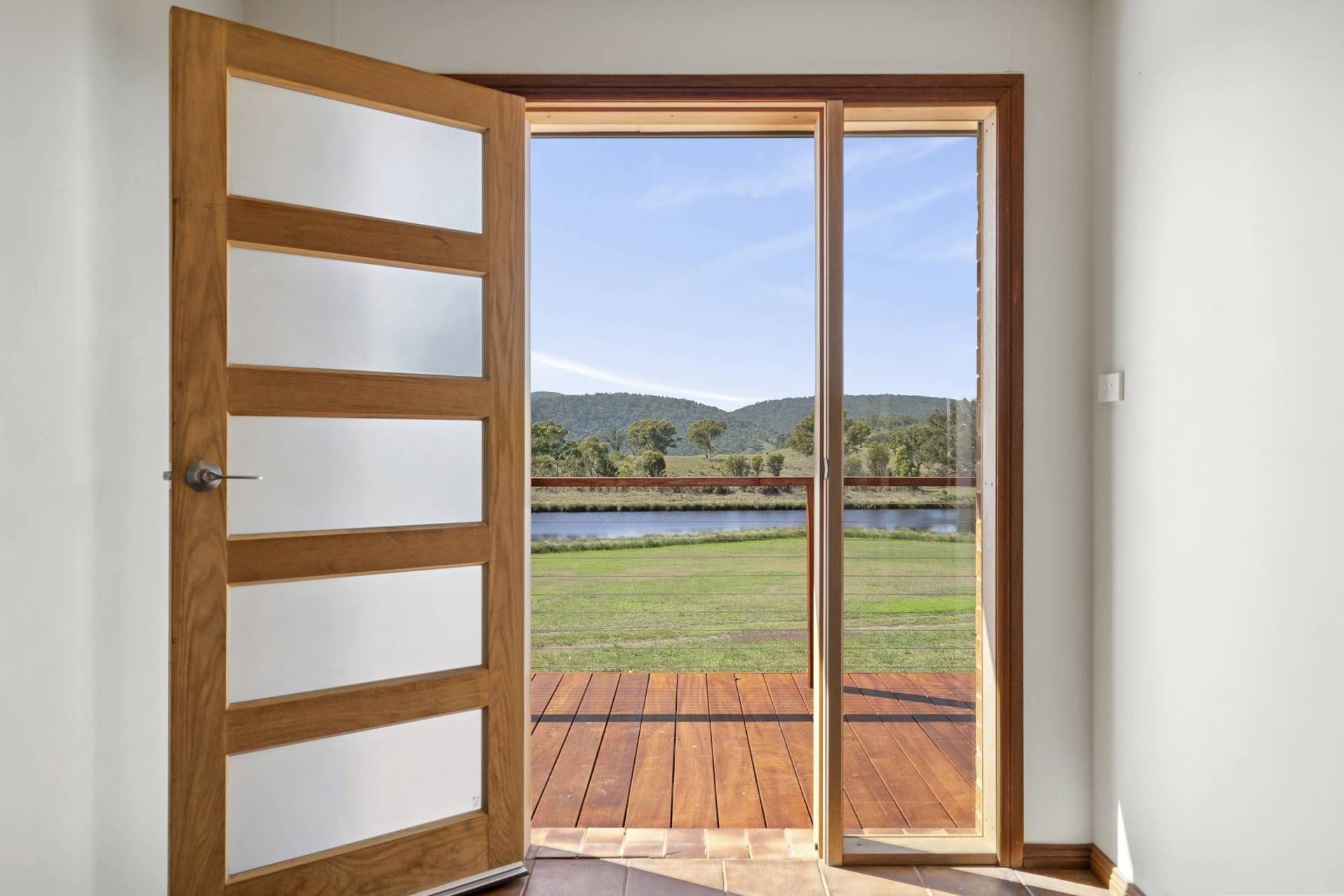 Wooden door with frosted glass panels opens onto a deck and green landscape under a blue sky — LD Carpentry in Goulburn, NSW