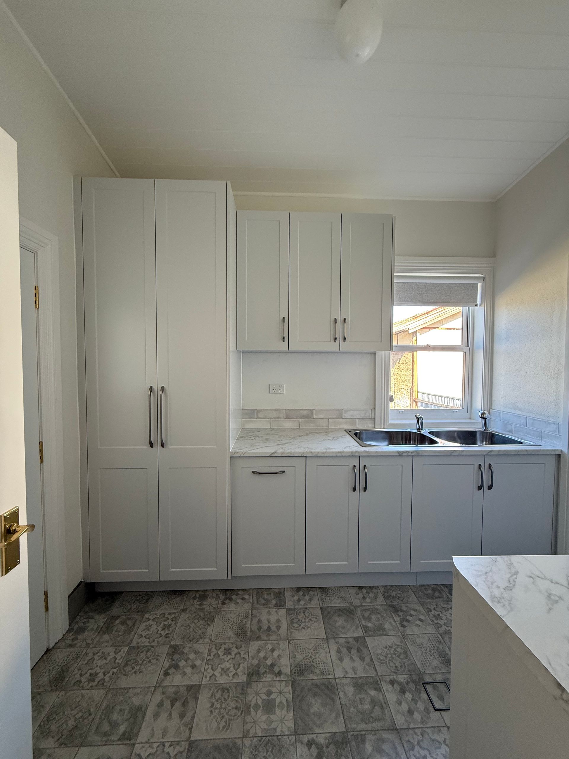 White kitchen with cabinets, countertops, and sink. Grey tiled floor — LD Carpentry in Goulburn, NSW