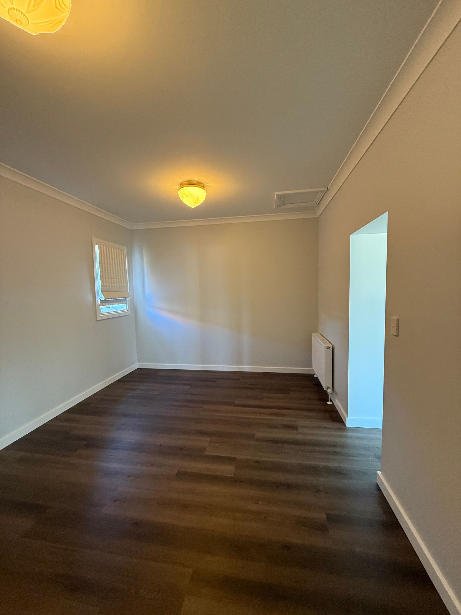 Empty room with dark wood-look flooring, white walls, crown molding, and a closed window — LD Carpentry in Goulburn, NSW