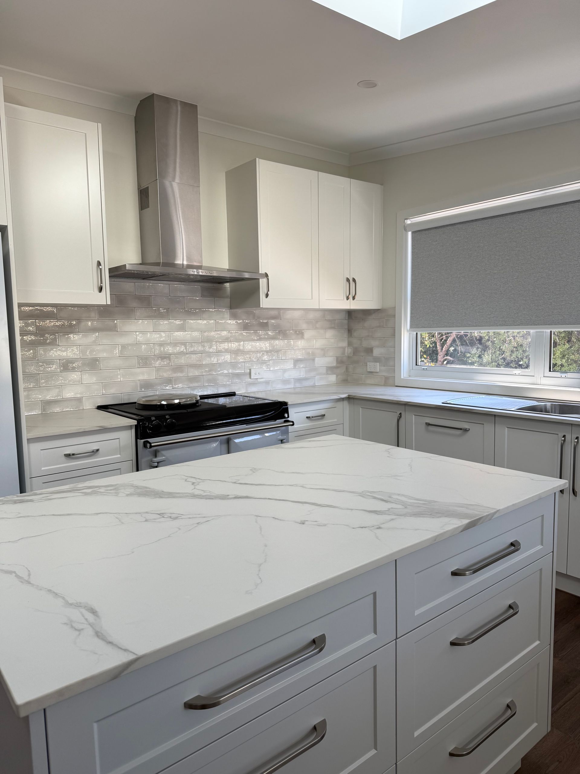 White kitchen with island, cabinets, and range. Marble countertops and gray backsplash — LD Carpentry in Goulburn, NSW