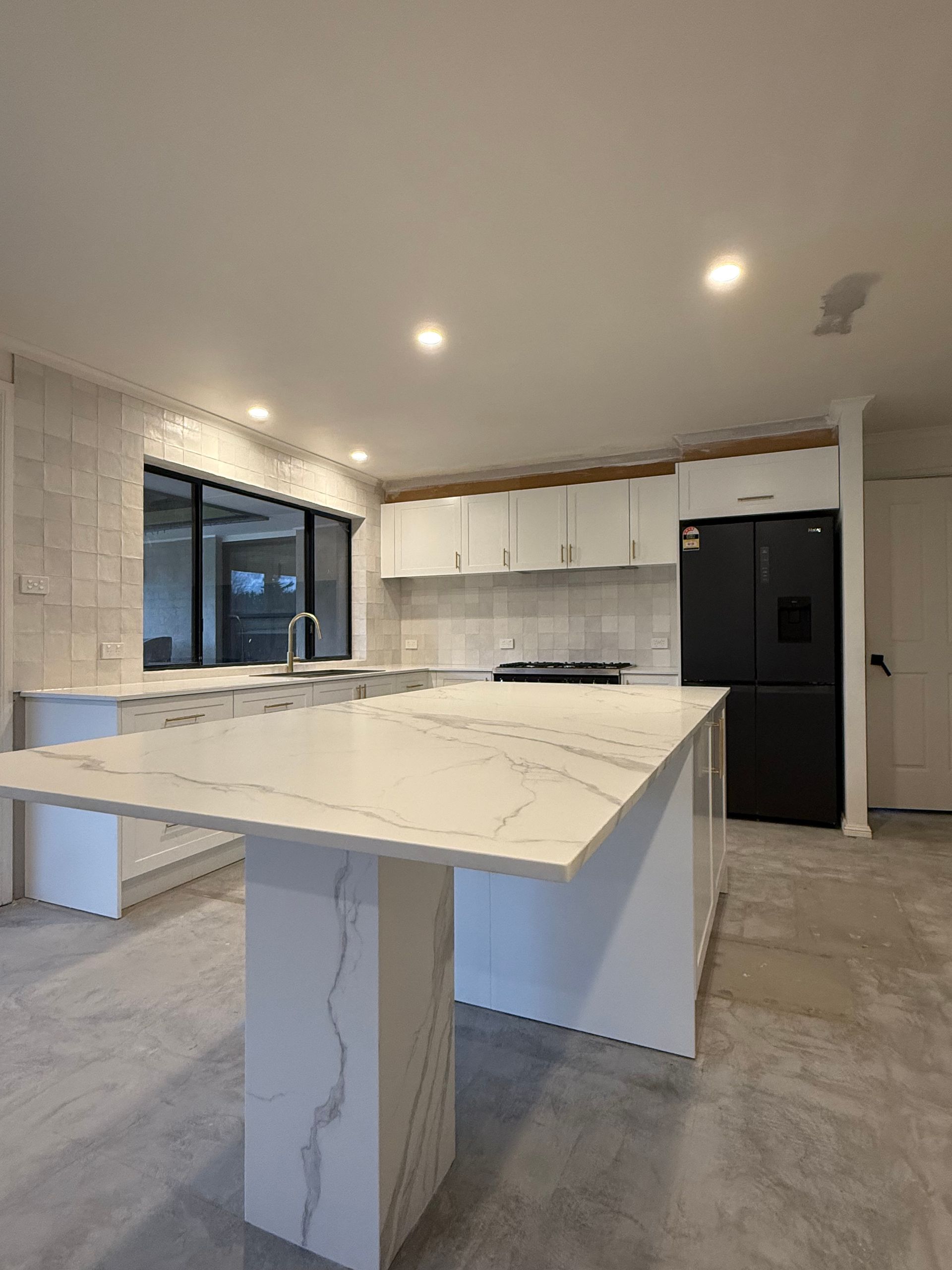 Modern kitchen with white marble island, black fridge, and white cabinets — LD Carpentry in Goulburn, NSW