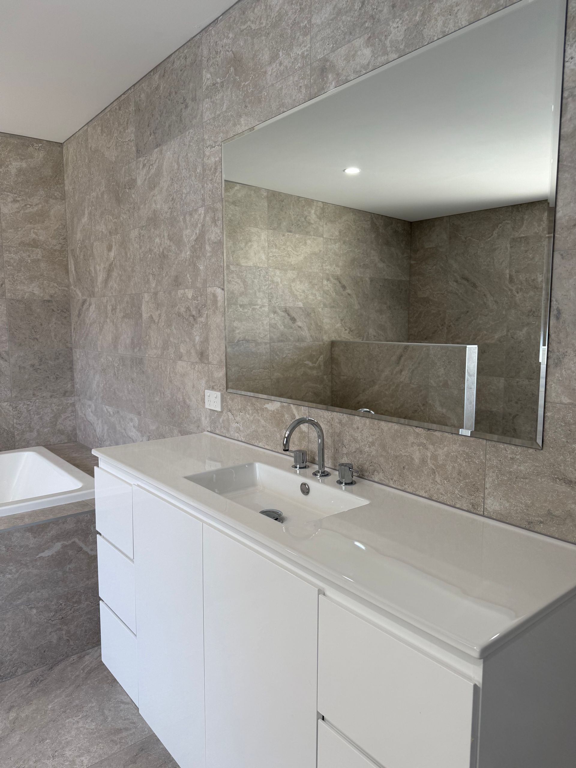 Bathroom with white vanity, sink, and large mirror; gray tiled walls and tub are visible — LD Carpentry in Goulburn, NSW