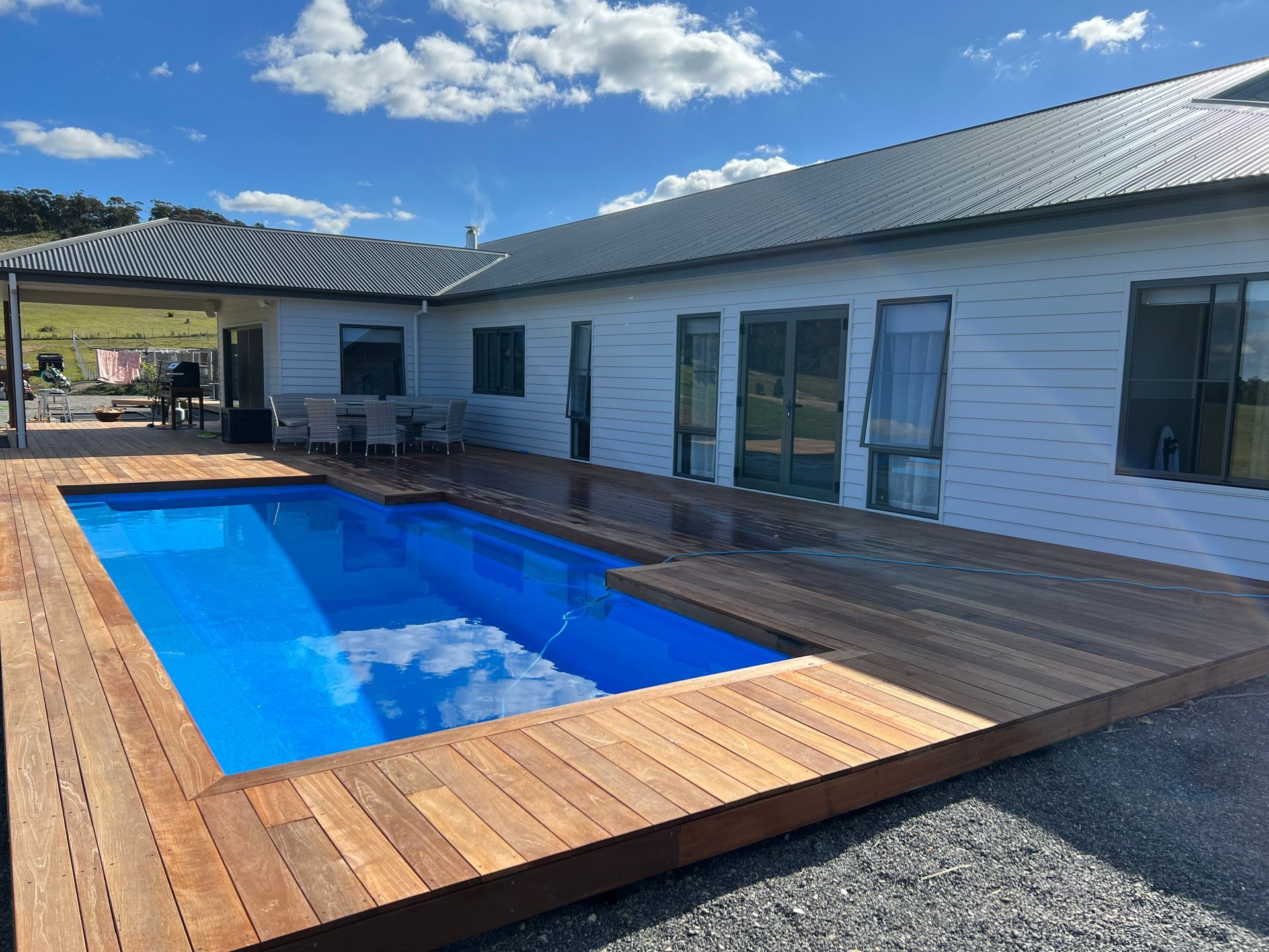 A rectangular swimming pool with wood decking next to a light-colored house under a blue sky — LD Carpentry in Goulburn, NSW