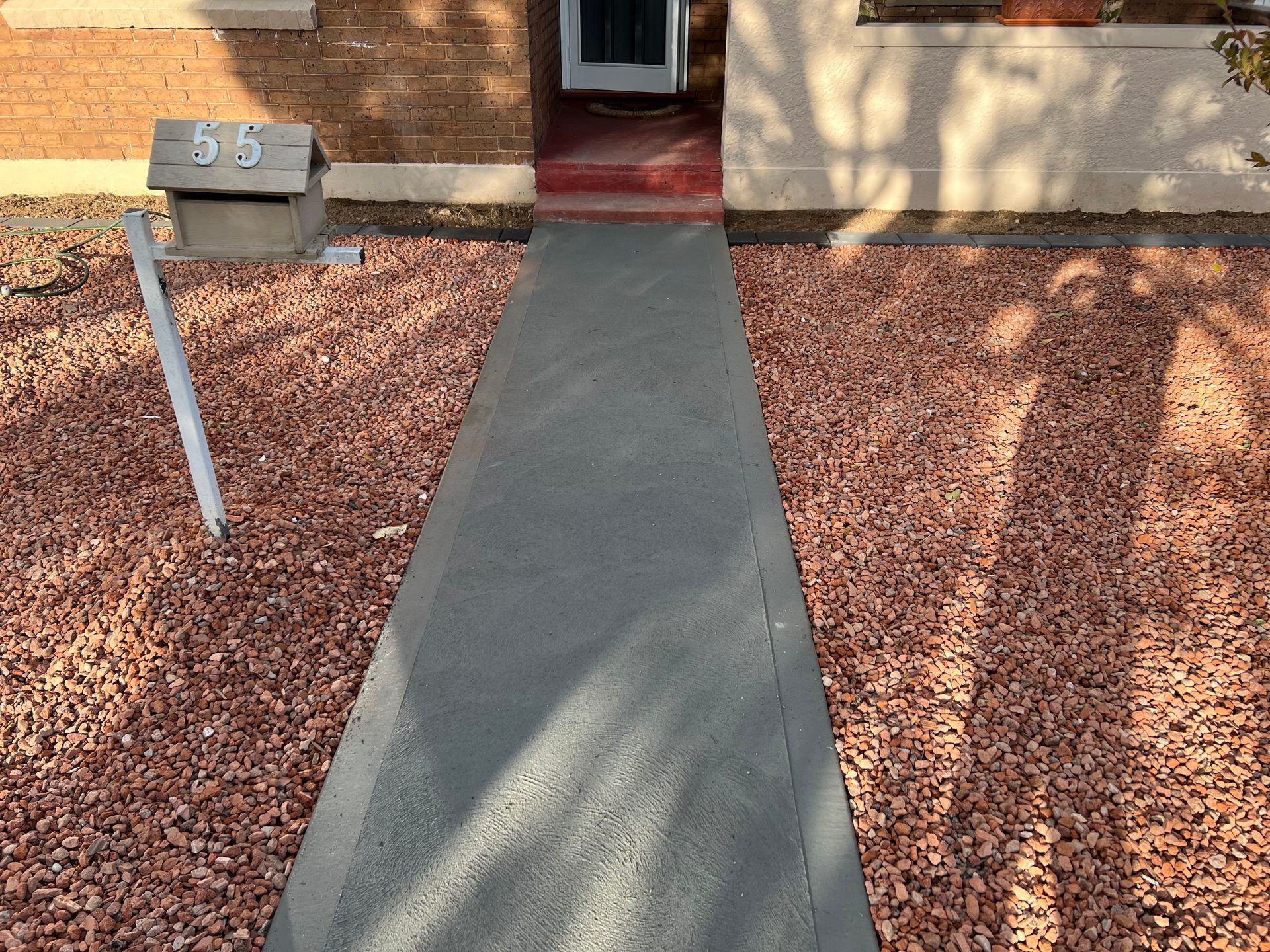 Concrete walkway leading to a red-doored house, surrounded by reddish-brown gravel — LD Carpentry in Goulburn, NSW