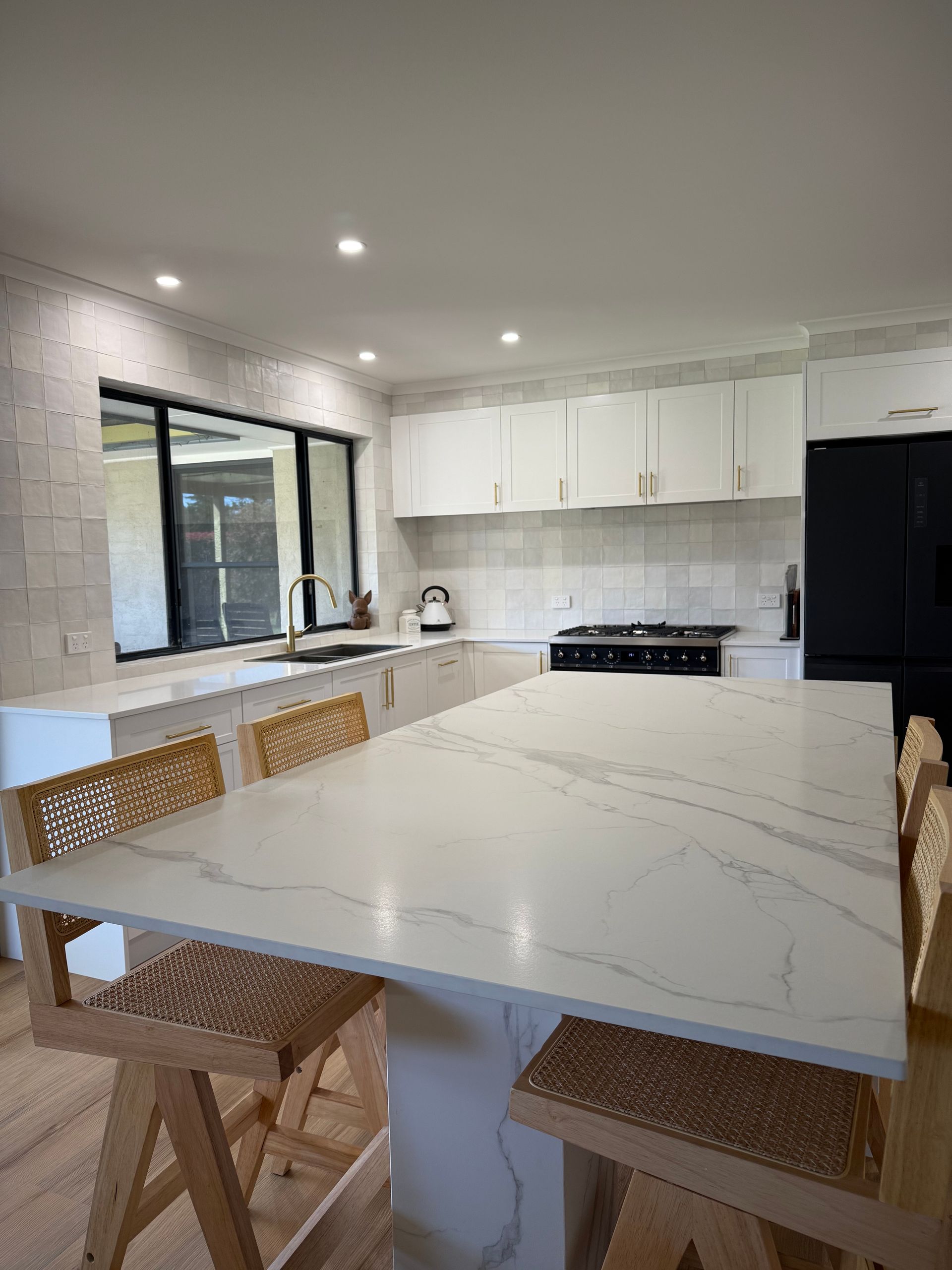 Modern white kitchen with a large island, marble countertop, and woven bar stools.