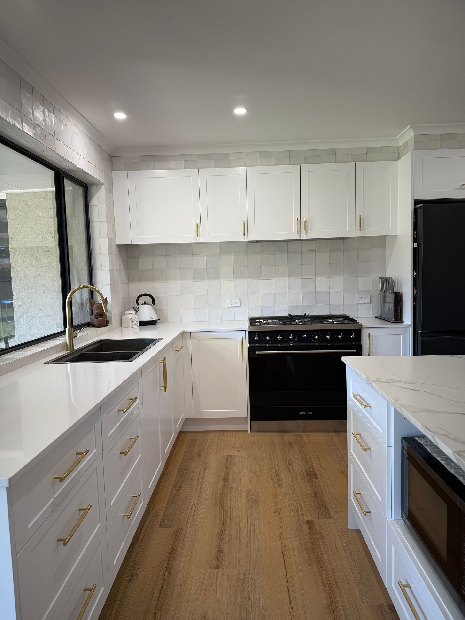 White kitchen with light wood floors, white counters, black stove, and gold hardware.