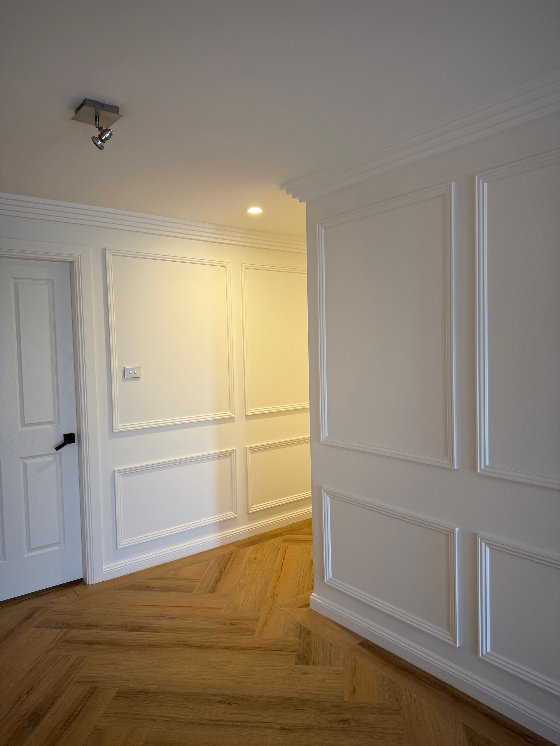 White paneled walls and door with wood floor, a doorway leads into the hallway.
