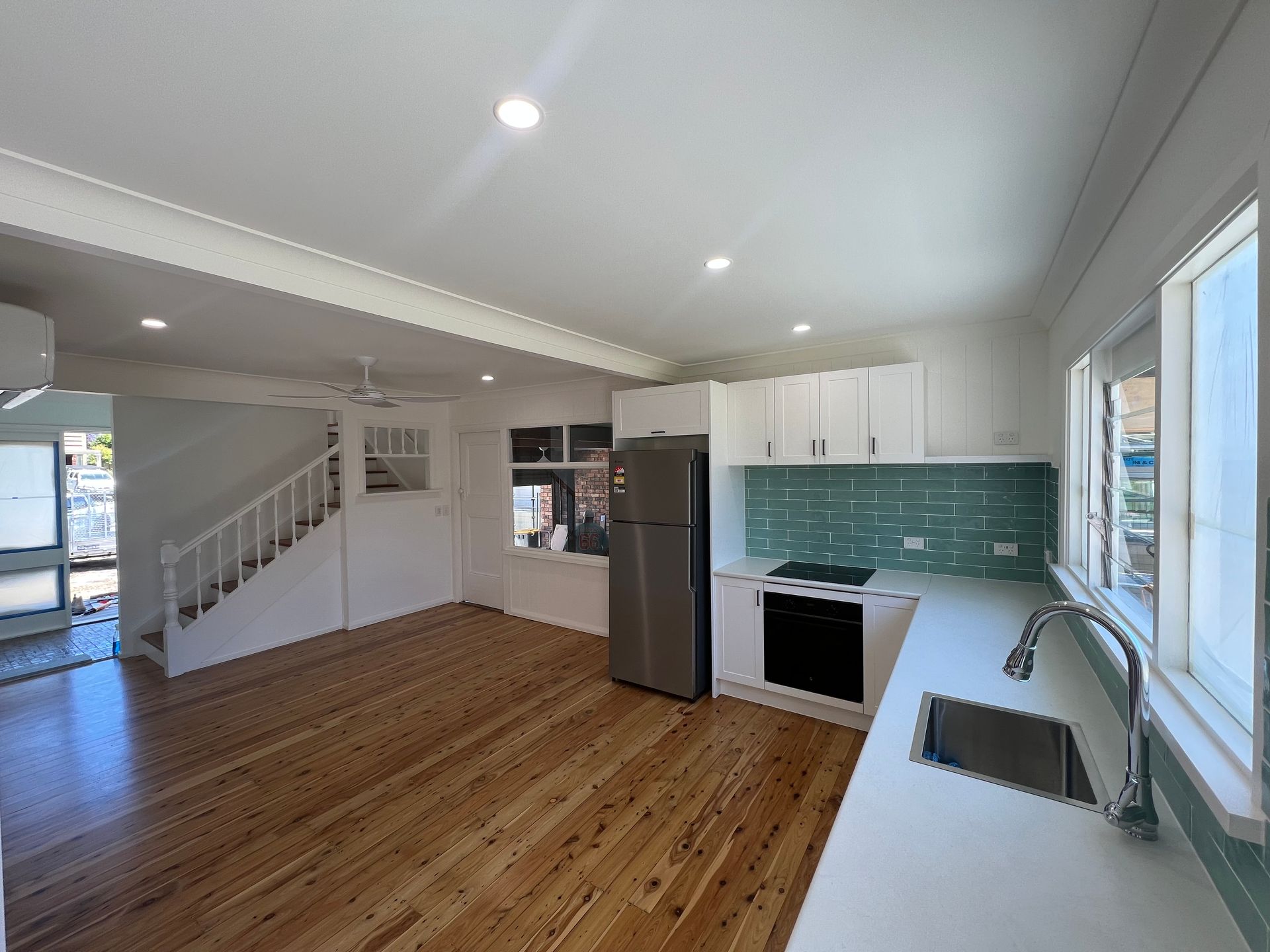 Kitchen with white cabinets, stainless steel fridge, wooden floor, and teal backsplash — LD Carpentry in Goulburn, NSW