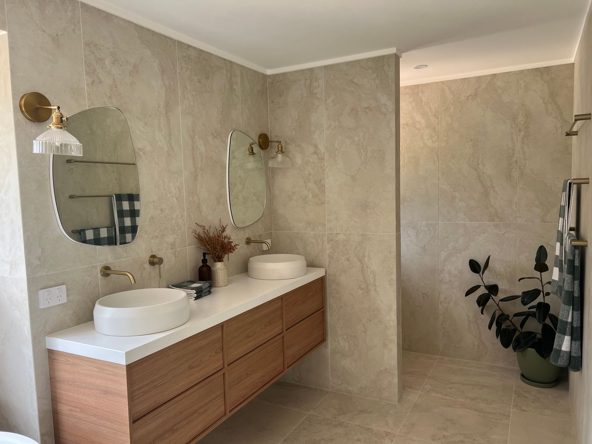 Bathroom with wood vanity, two vessel sinks, gold fixtures, beige tile walls, and a plant — LD Carpentry in Goulburn, NSW