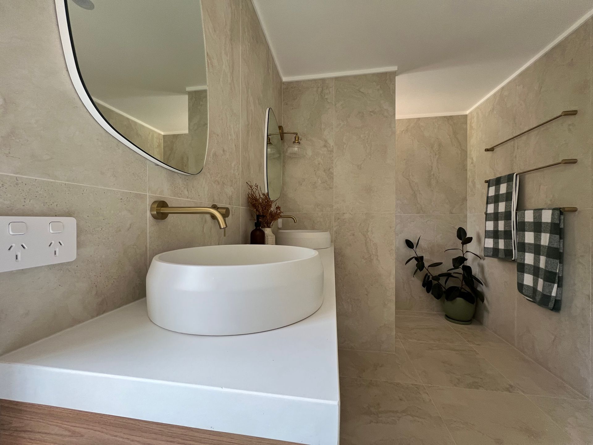 Modern bathroom with white sink, gold fixtures, beige tiles, and checkered towels — LD Carpentry in Goulburn, NSW