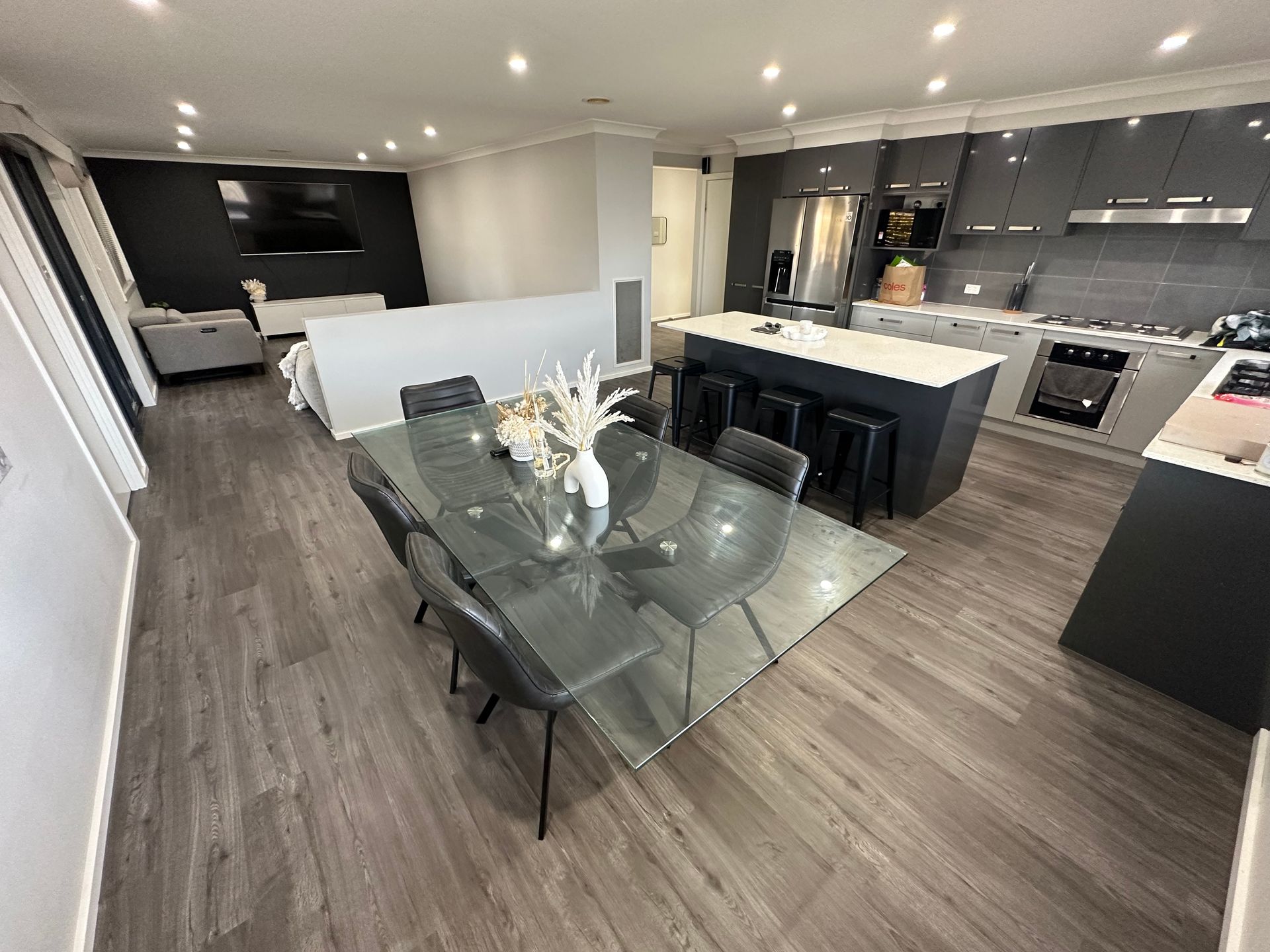 Open-concept kitchen and dining room with glass table, island, and dark gray cabinets — LD Carpentry in Goulburn, NSW