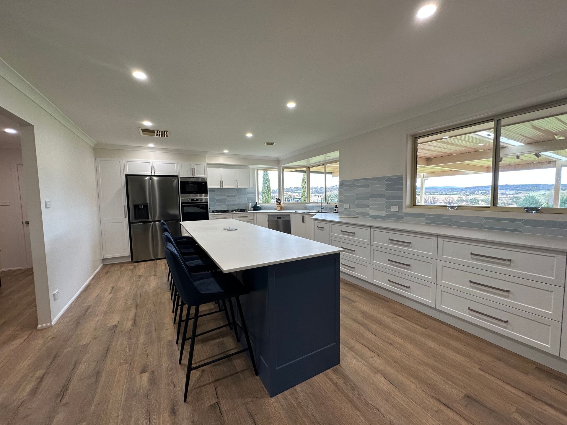 Modern kitchen with white cabinetry, blue island, wood floors, and a scenic view — LD Carpentry in Goulburn, NSW