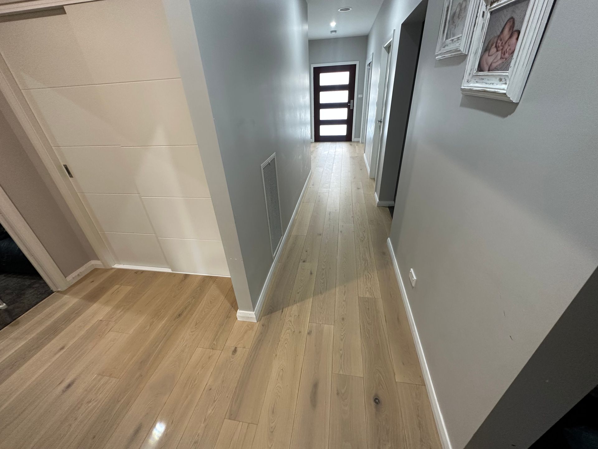 Narrow hallway with wood floor, gray walls, white trim, and black door at end — LD Carpentry in Goulburn, NSW