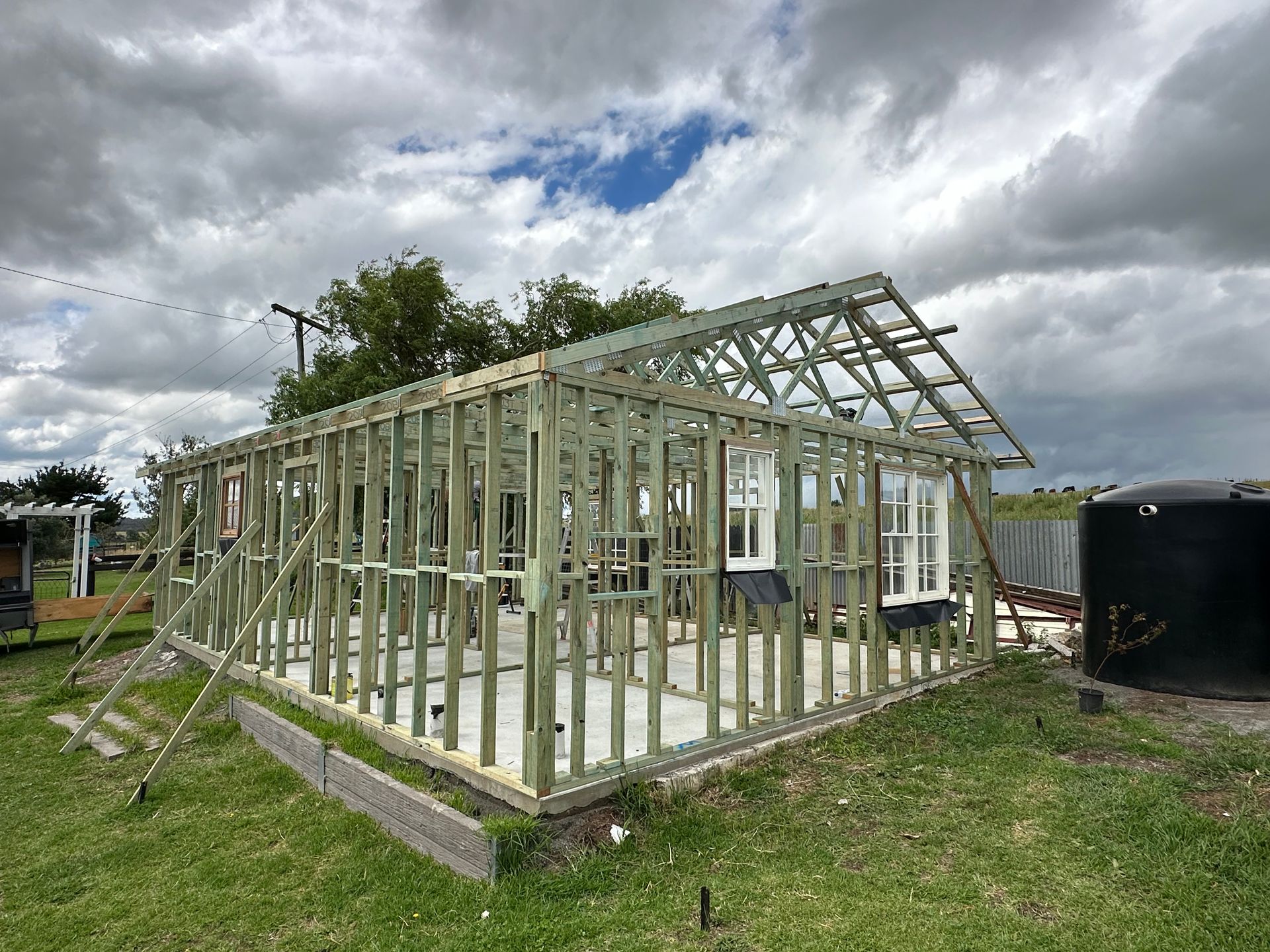 Wooden frame of a building under construction in a grassy field, with a cloudy sky overhead — LD Carpentry in Goulburn, NSW
