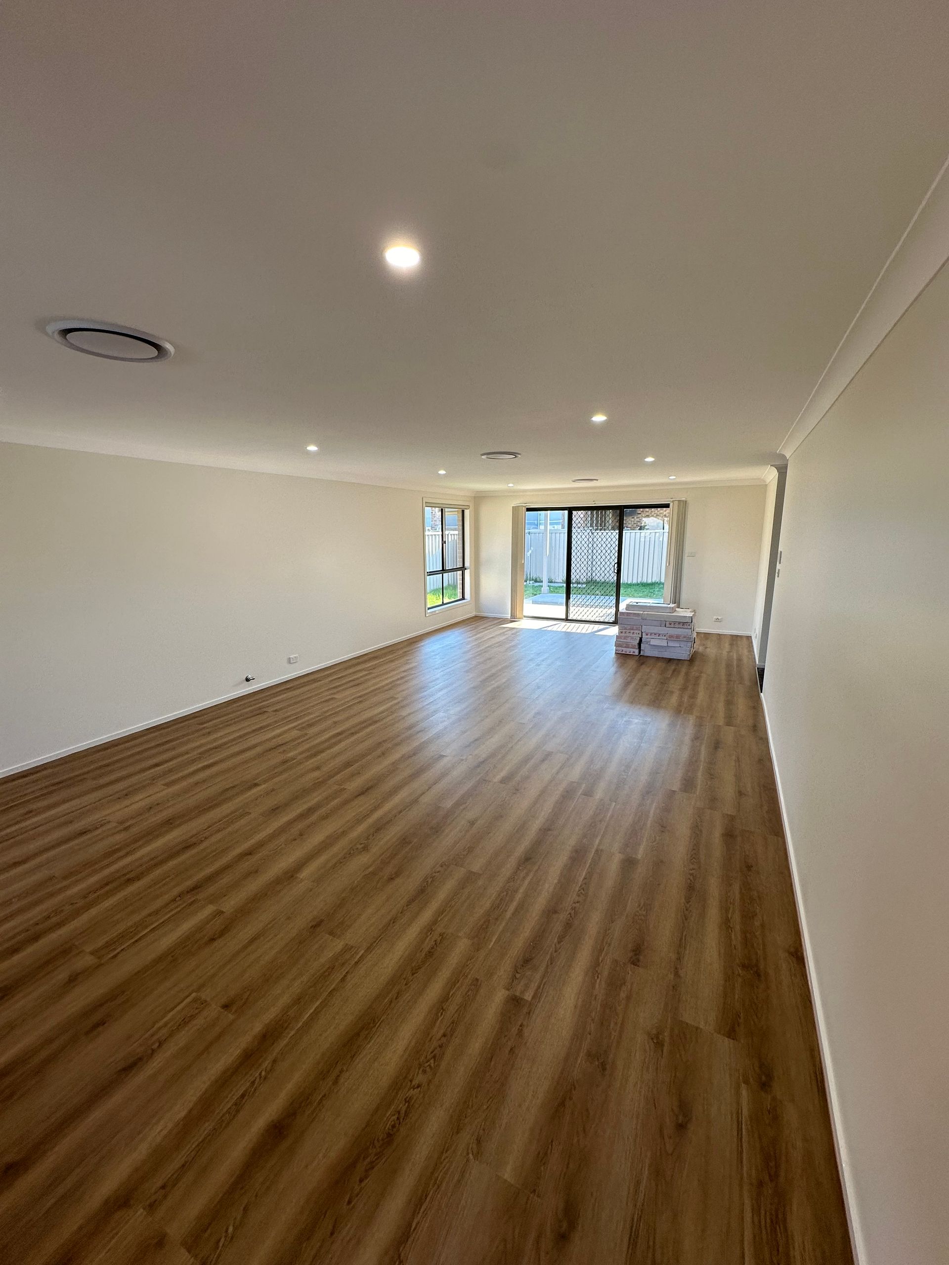 Empty living room with wood-look flooring, white walls, and a glass door to the outside — LD Carpentry in Goulburn, NSW