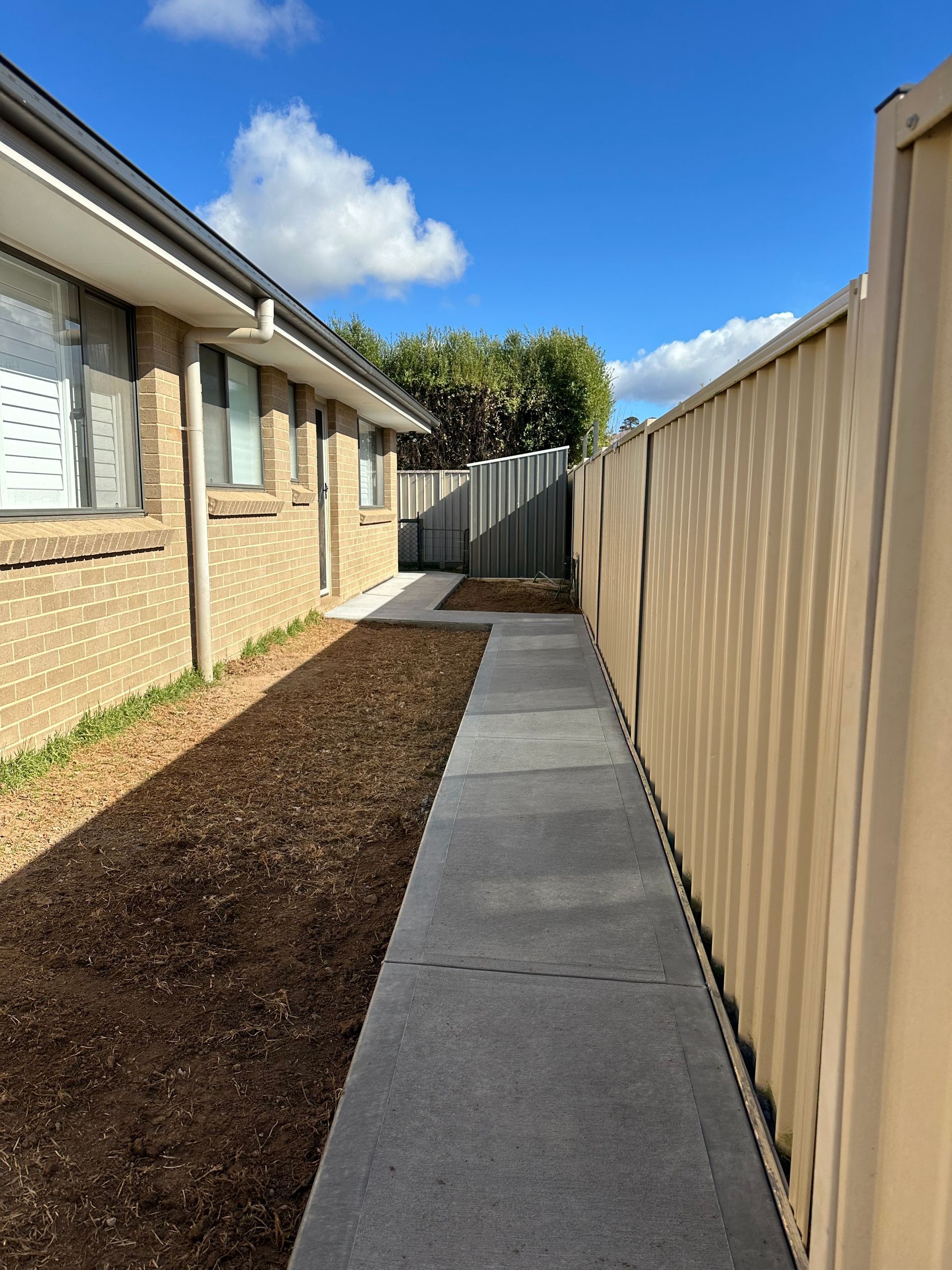 Narrow pathway between a brick building and tan fence; blue sky — LD Carpentry in Goulburn, NSW