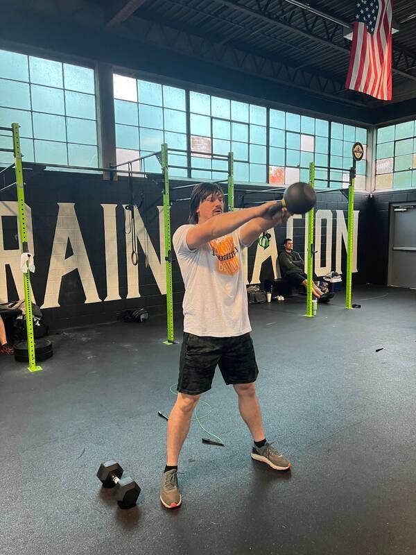A man is swinging a kettlebell in front of a sign that says raination