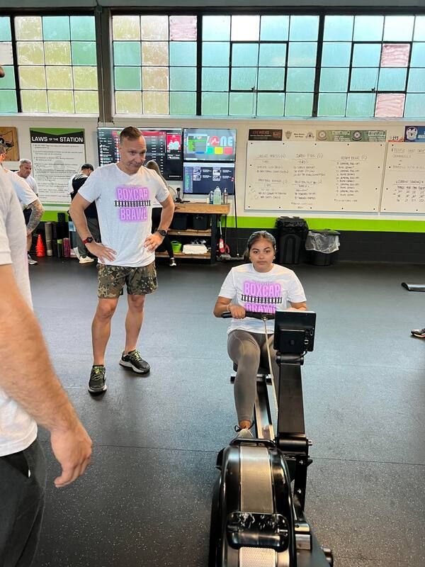 A woman is riding a rowing machine in a gym while a man watches.