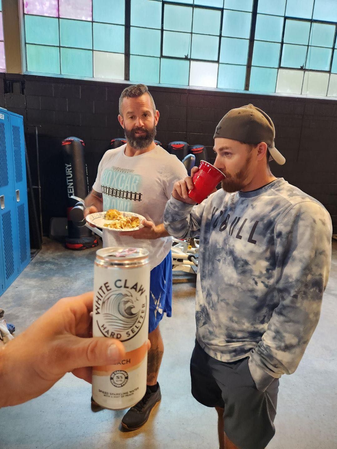 A man is holding a can of white claw beer while another man holds a plate of food.