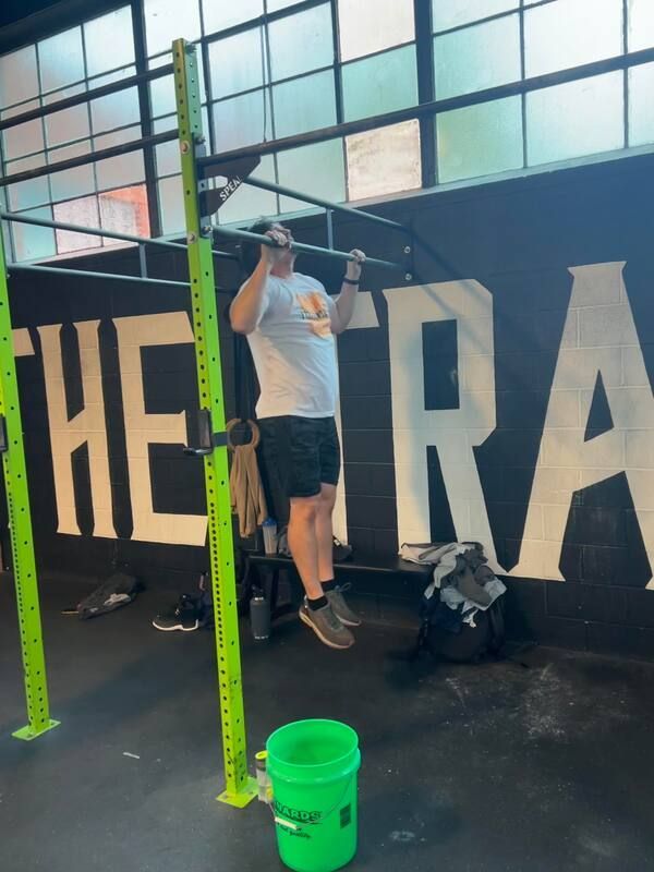 A man is doing pull ups in front of a sign that says the tra