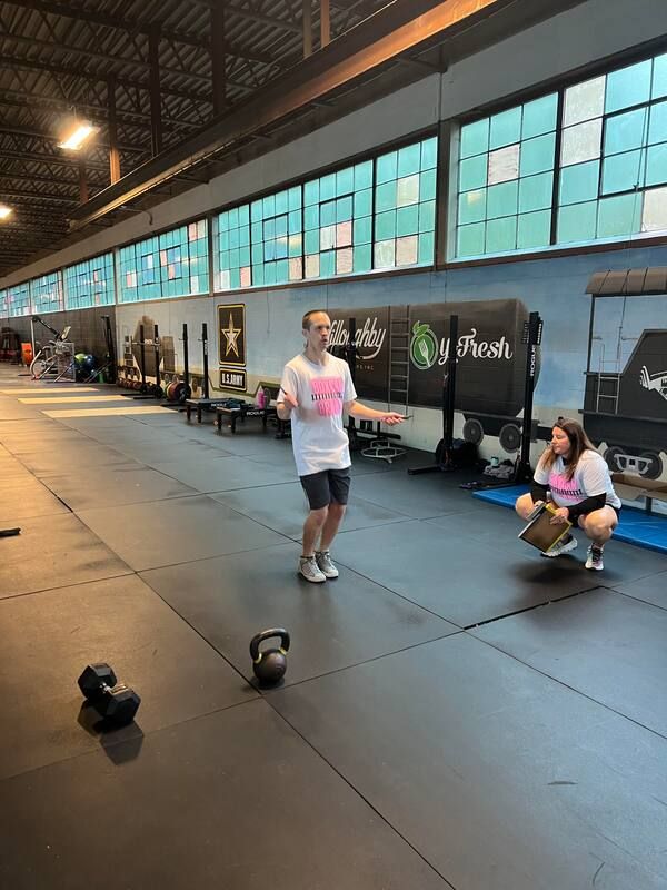 A man is jumping a jump rope in a gym while a woman squats next to him.