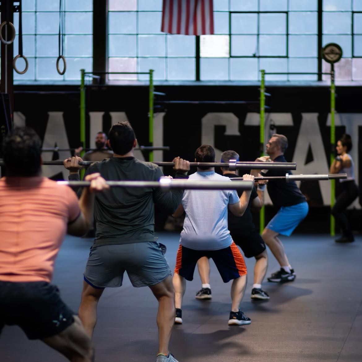 A group of people are squatting with barbells in front of a sign that says all star