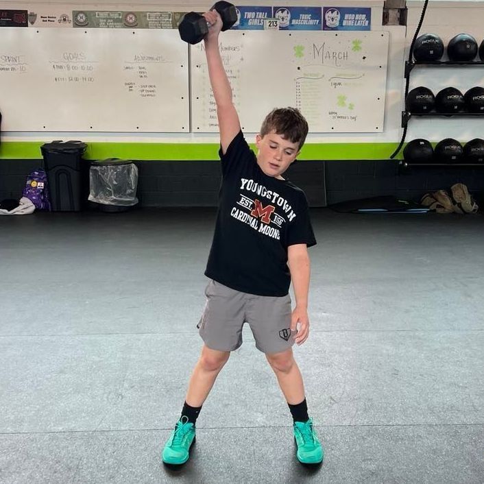 A young boy is lifting a kettlebell in a gym.
