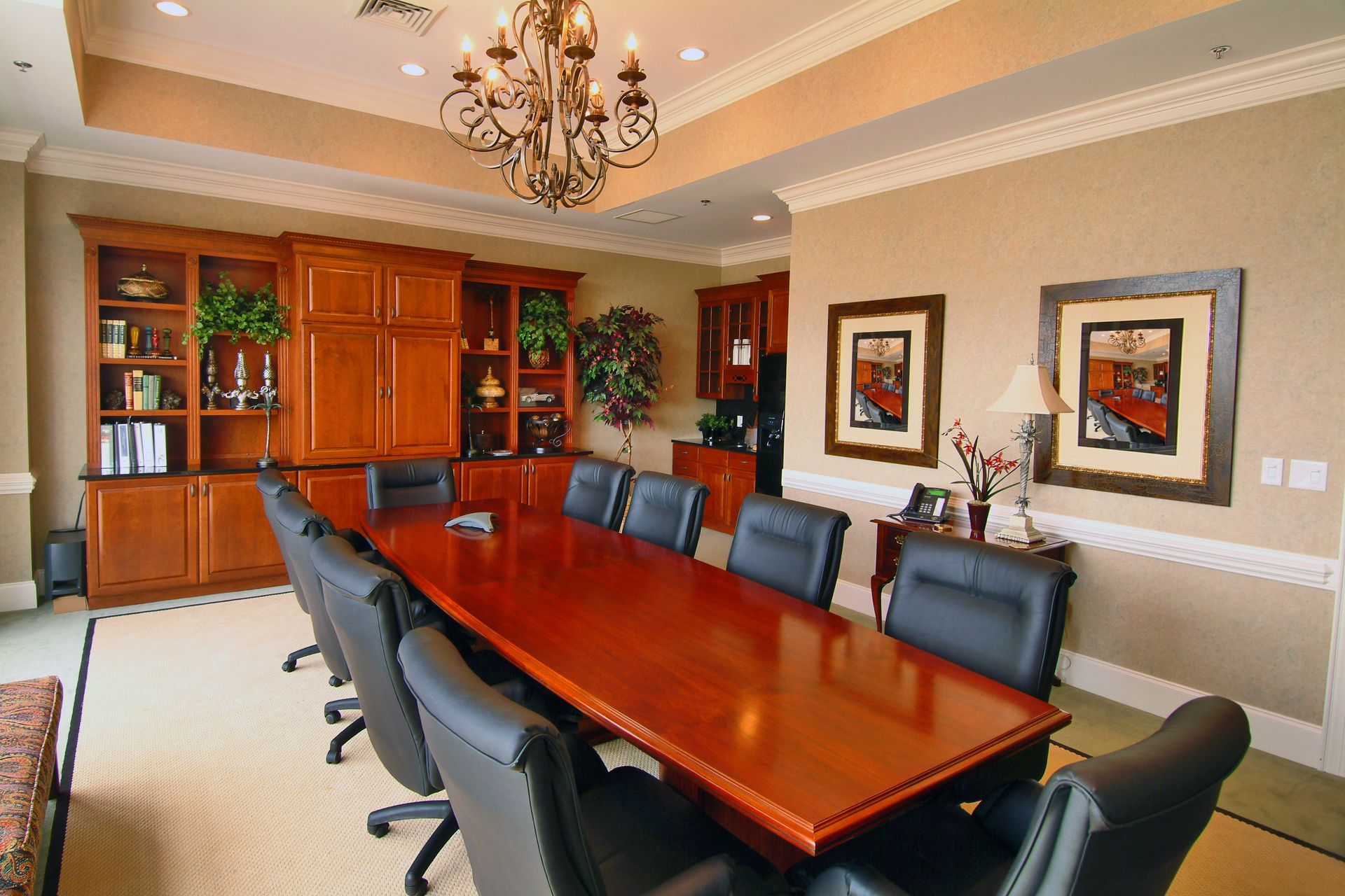 A well-lit office conference room with a large wooden table, leather chairs, and built-in wooden cabinetry.