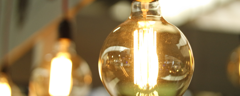 Close-up of a lit Edison light bulb, with other bulbs blurred in the background, creating a warm ambiance.