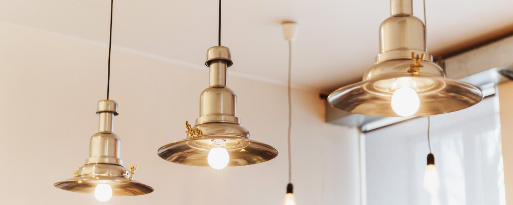 Four brass pendant lights hanging from a white ceiling, each with a bright lightbulb.