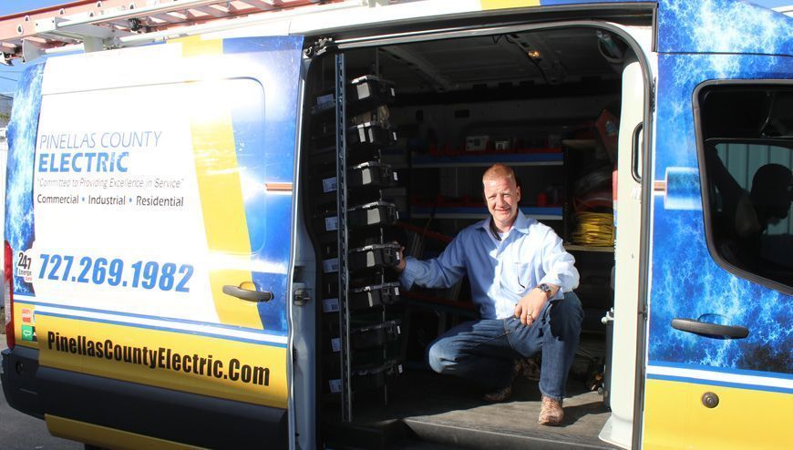 Man kneels in an open electric company van. The van has the company logo, and contact info.
