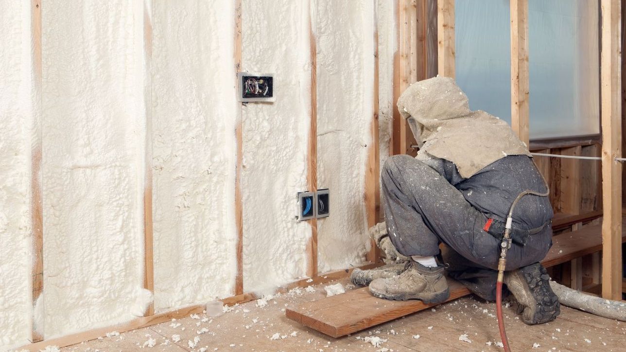 A man is spraying insulation on a wall in a room.