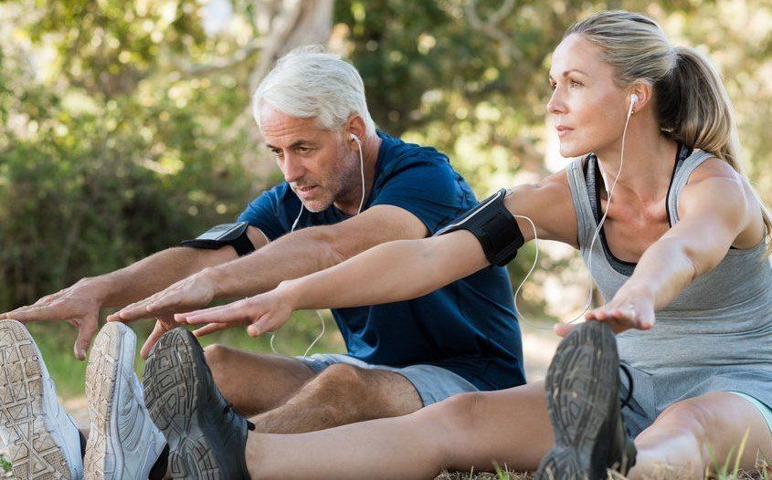 A man and a woman are stretching their legs in a park.