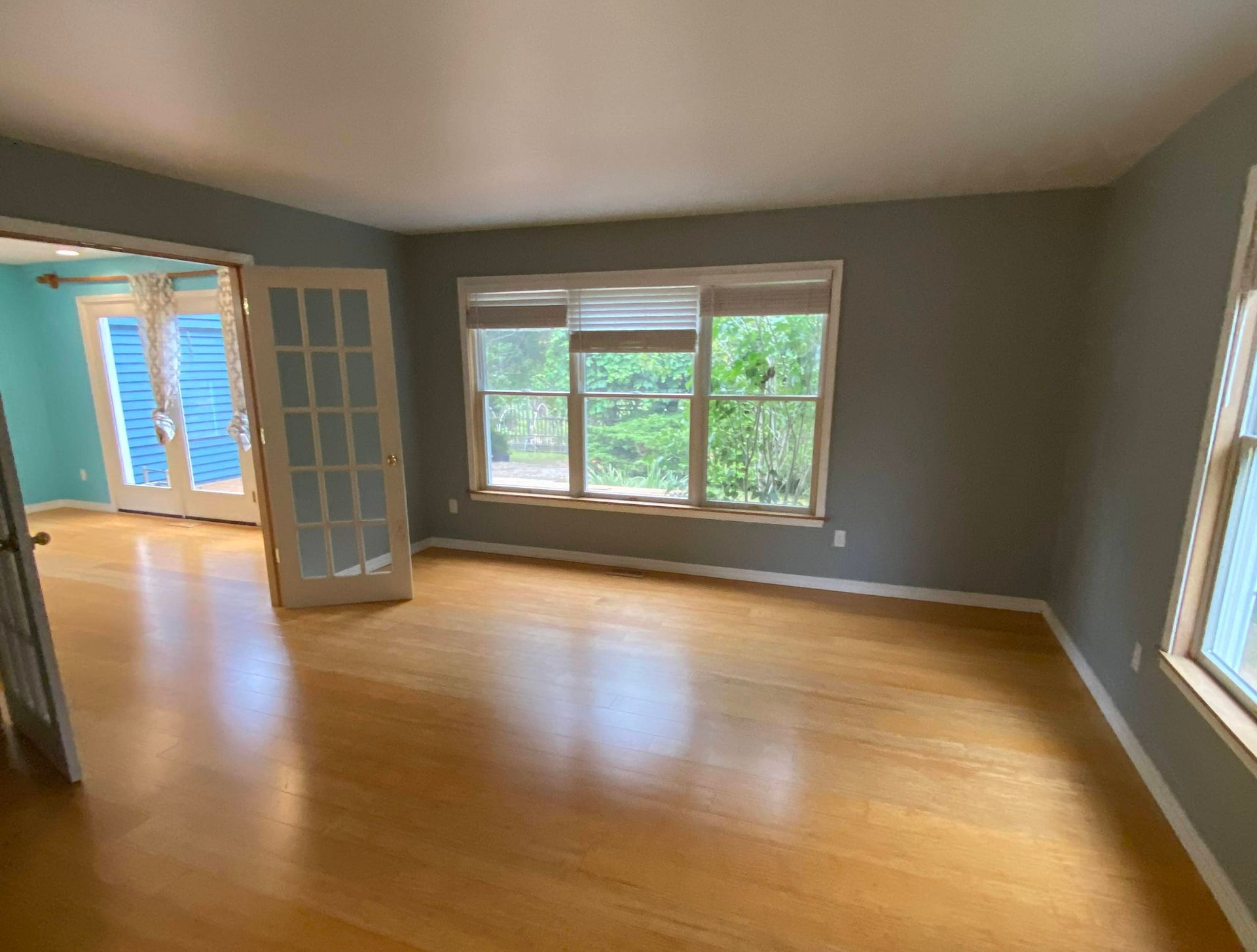 Empty room with hardwood floors, gray walls, and large windows.